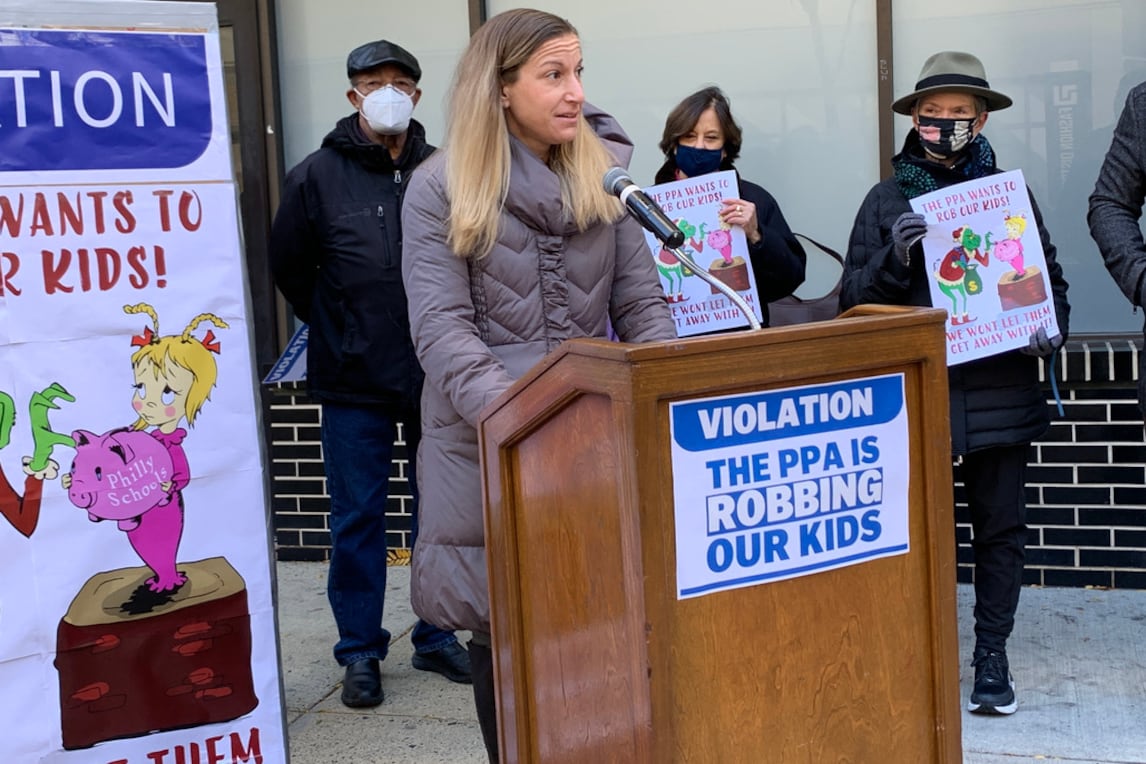 Wearing a coat in the cold and speaking at a podium a representative from the teachers union addresses a rally.