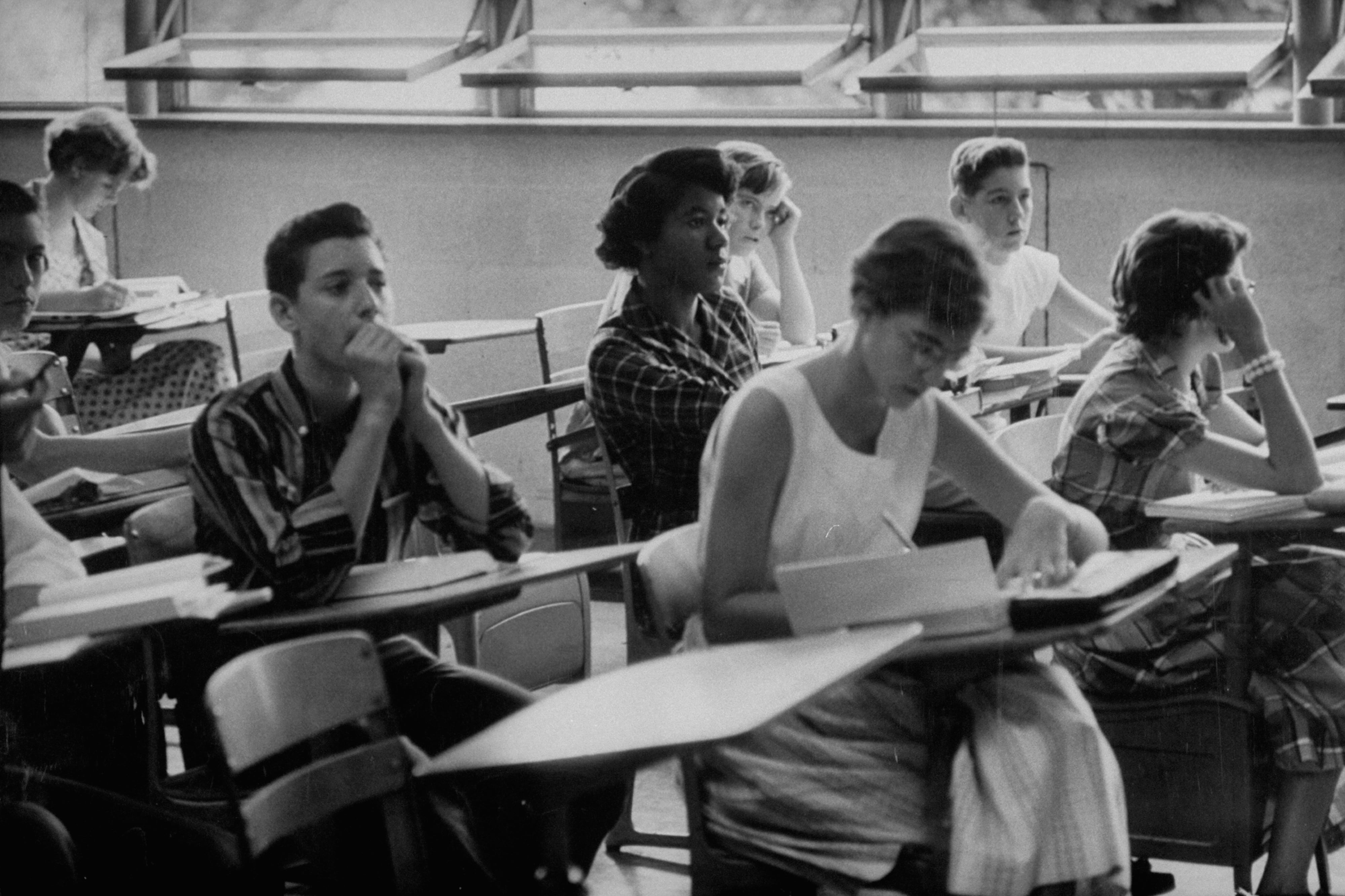 In this historic black and white photograph, one young Black woman sits in the middle of a high school class alongside several white students, after the school was desegregated in Tennessee.