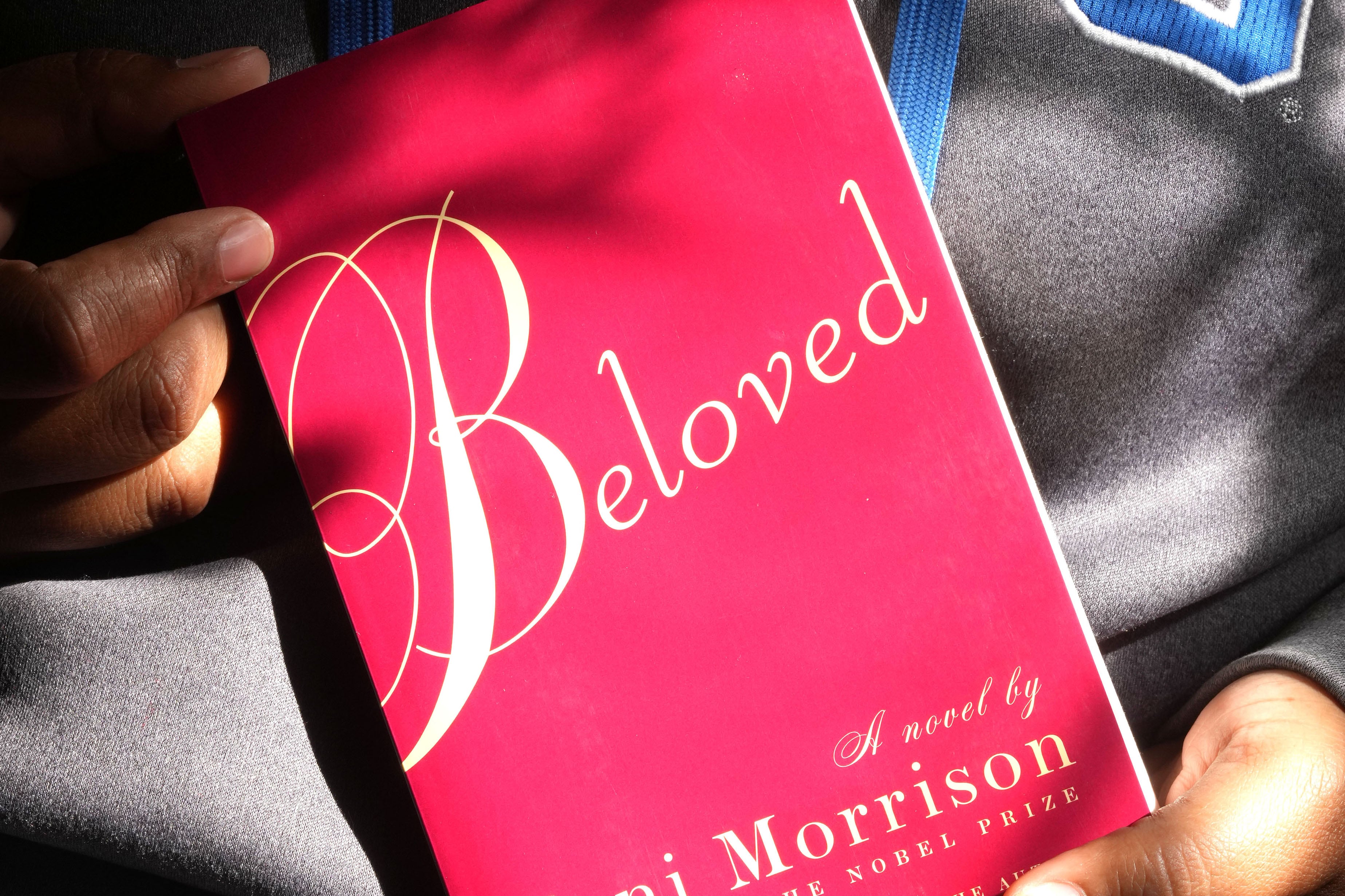 A pair of hands holds a red book with large, white letters that read "Beloved."