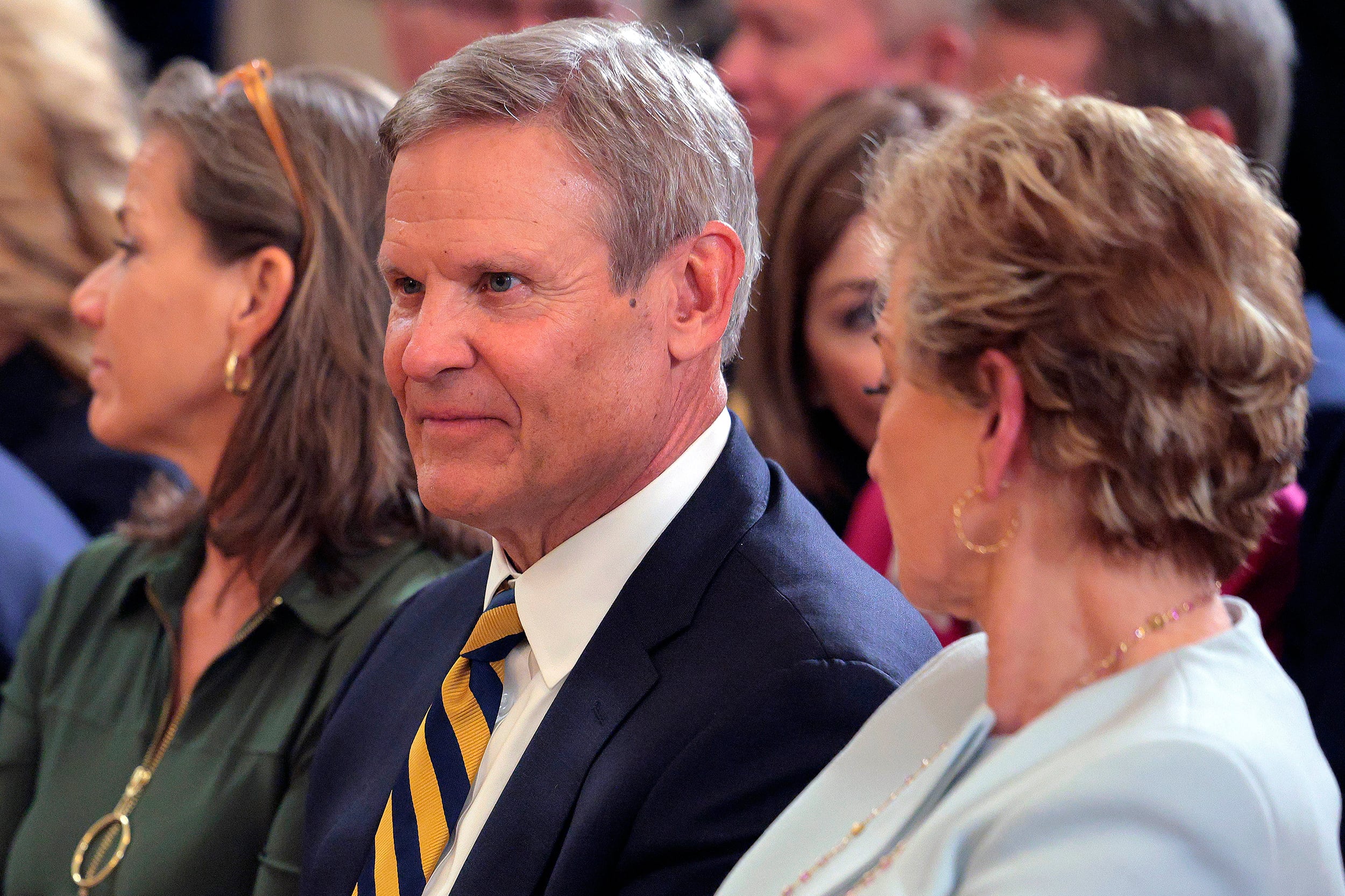 A photograph of three people in suits sitting next to each other in a sea of a larger group of people.