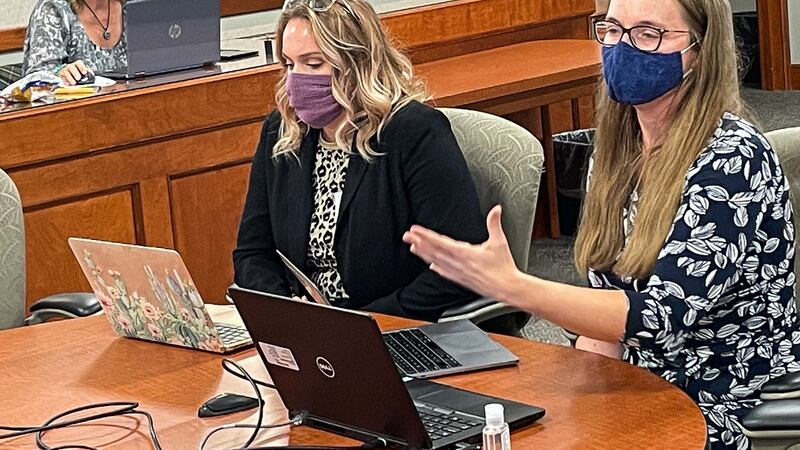 Michigan Teacher of the Year Leah Porter  addresses the state Board of Education during an October meeting. She is seated at the head of a conference table with Kacie Hook of Roscommon Middle School, who is the Teacher of the Year for Region 2. Both have open laptops in front of them.