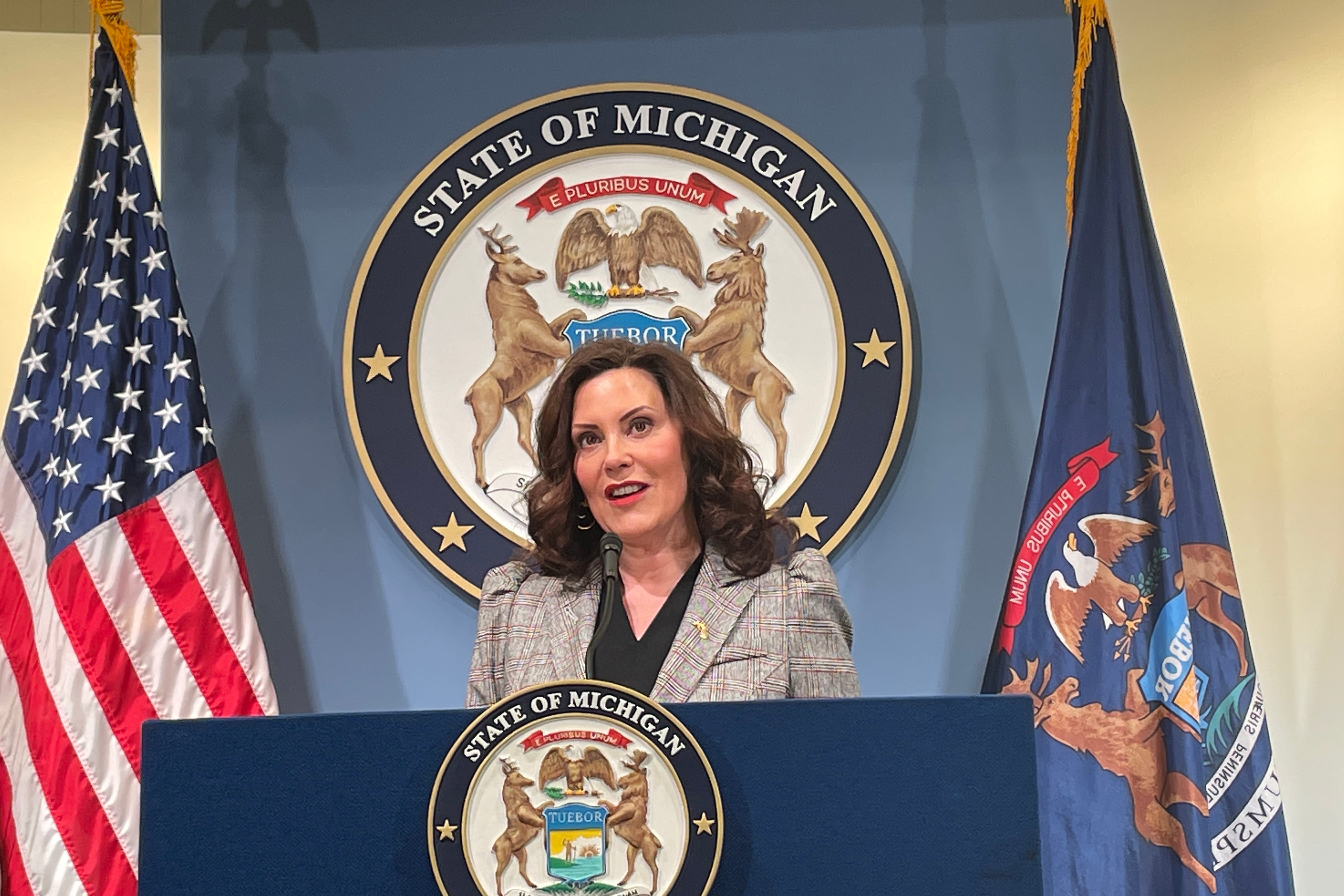 Gov. Gretchen Whitmer stands in front of a podium while talking to reporters.