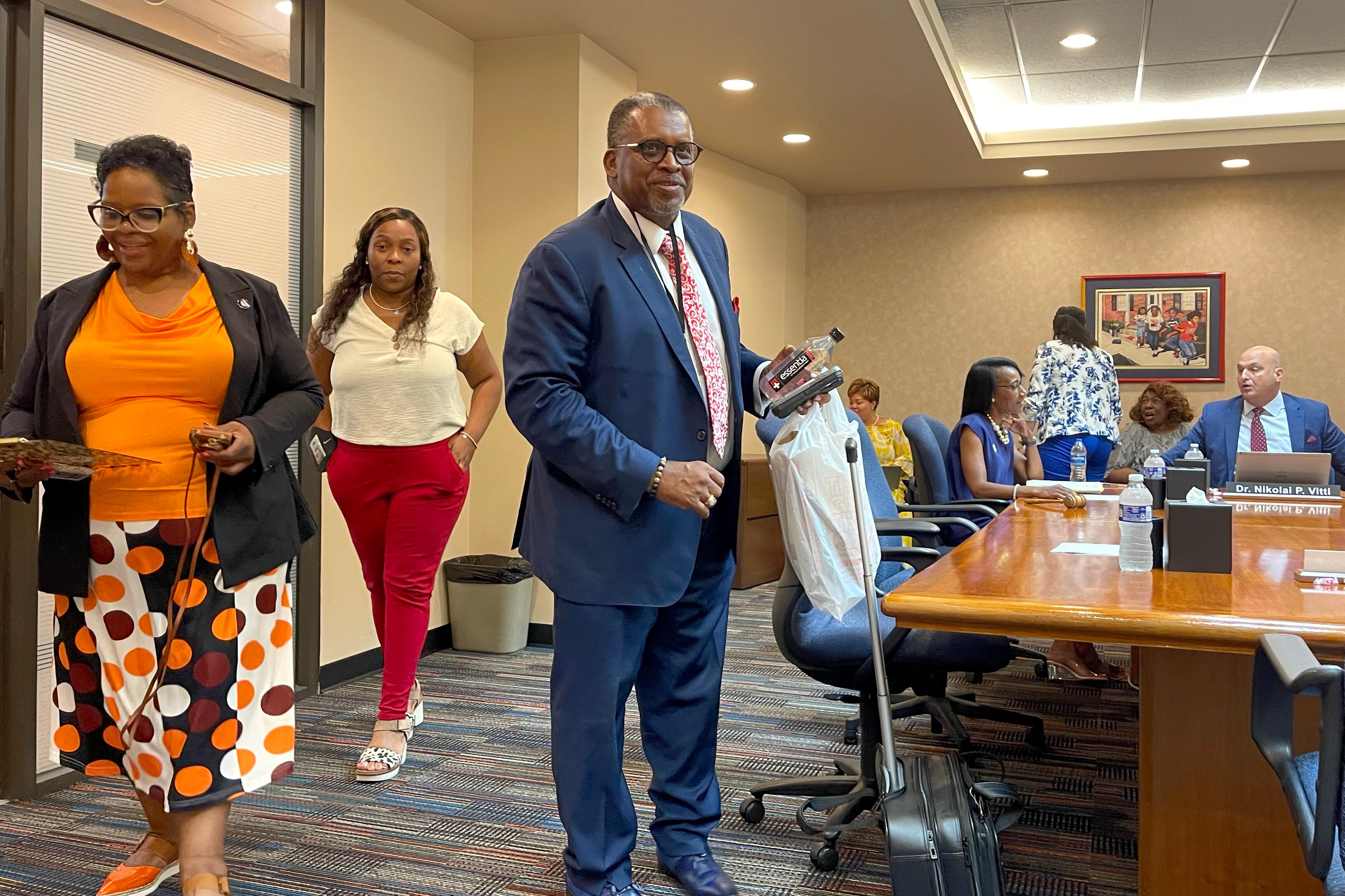 A photograph of several adults in business clothes standing around a rectangular meeting room table in a conference room.