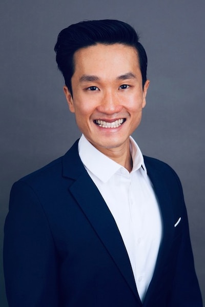A man in a blue suit poses for a portrait in front of a blue background.