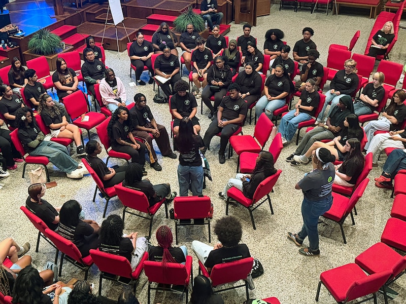 A group of students sit in red chairs shot from above.