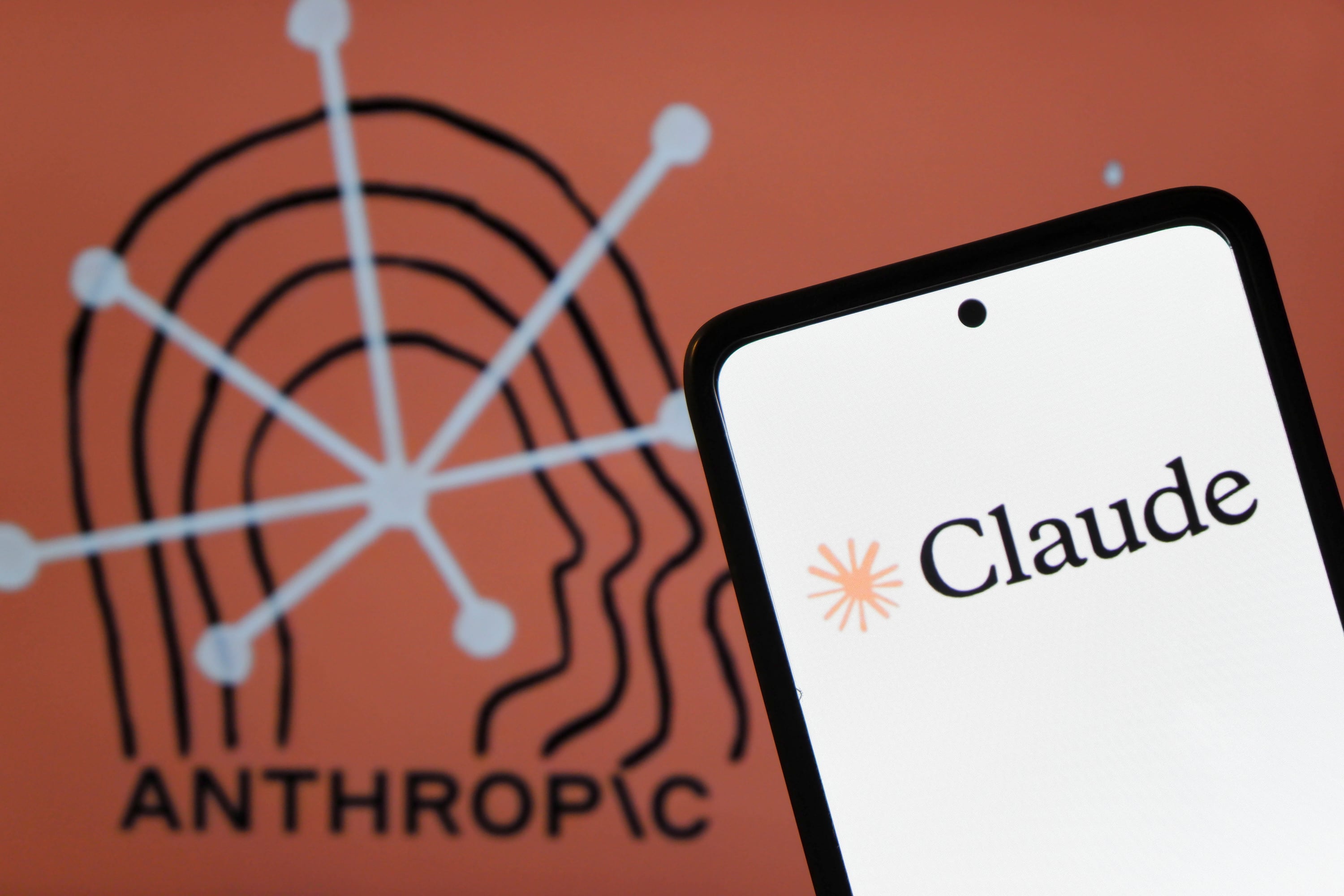 A phone on the right with the logo of an AI tool, Claude, and in the far background, it's the company's name Anthropic.