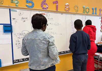 Two teachers and a student work at a dry erase board in a classroom.