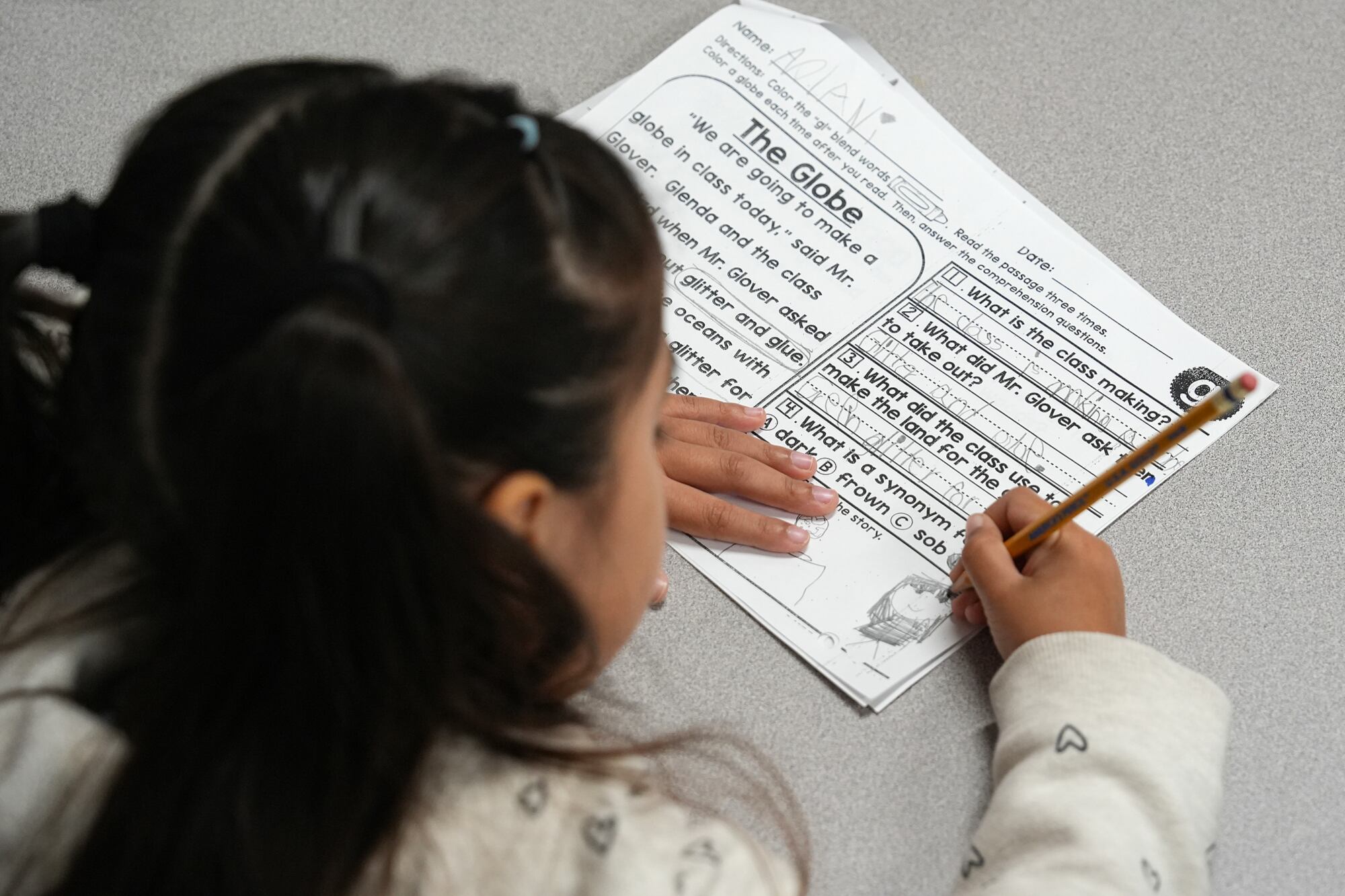 a girl writes with a pencil on a worksheet