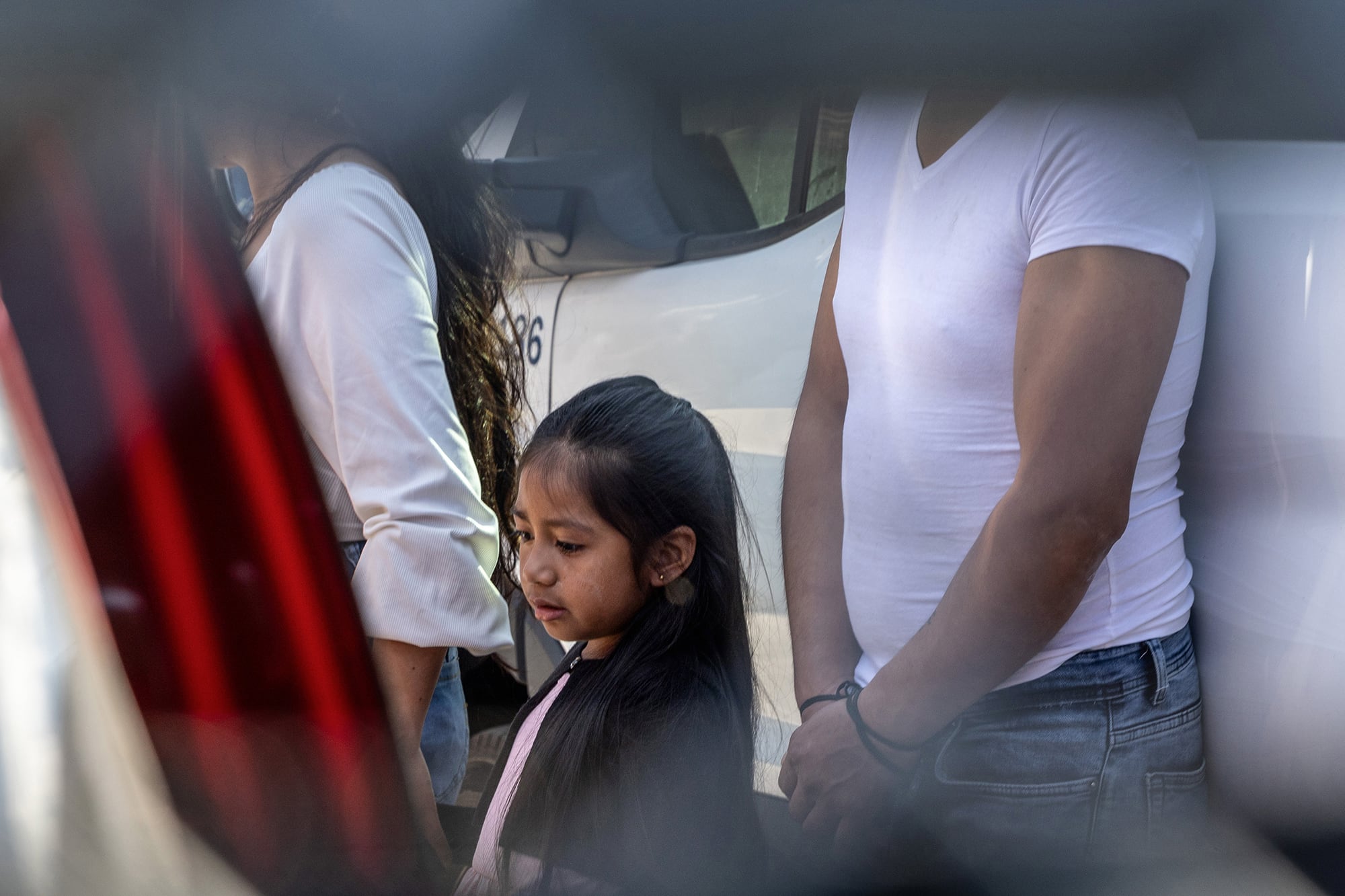 A photograph of a young girl standing next to adults outside.