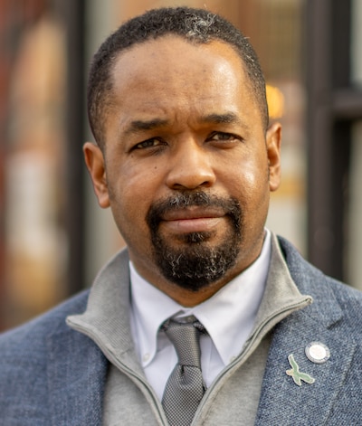 A mugshot of a man in a gray jacket, gray sweat jacket, white shirt and gray tie.