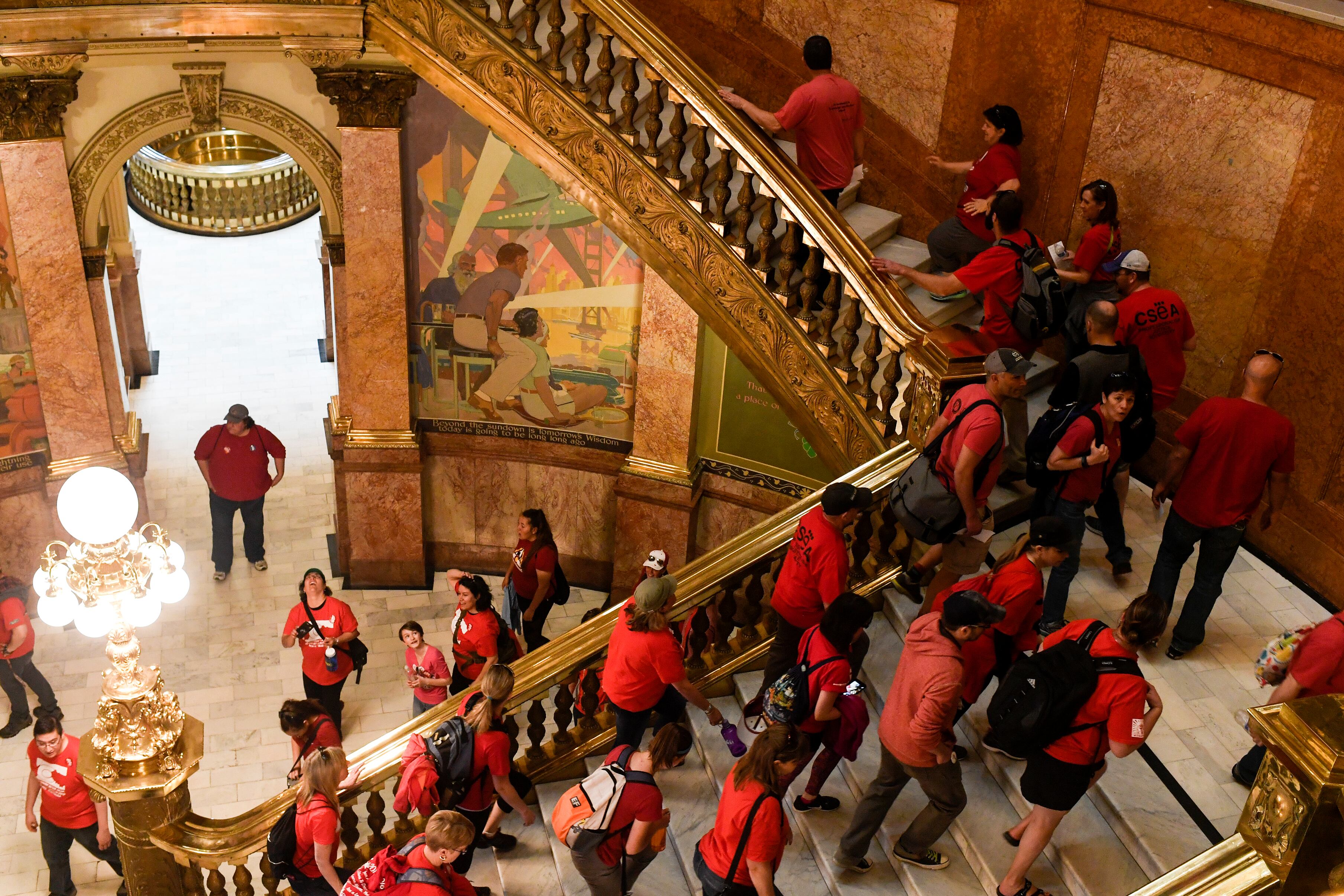 A large group of people in red walk up a set of Capitol building stairs inside.