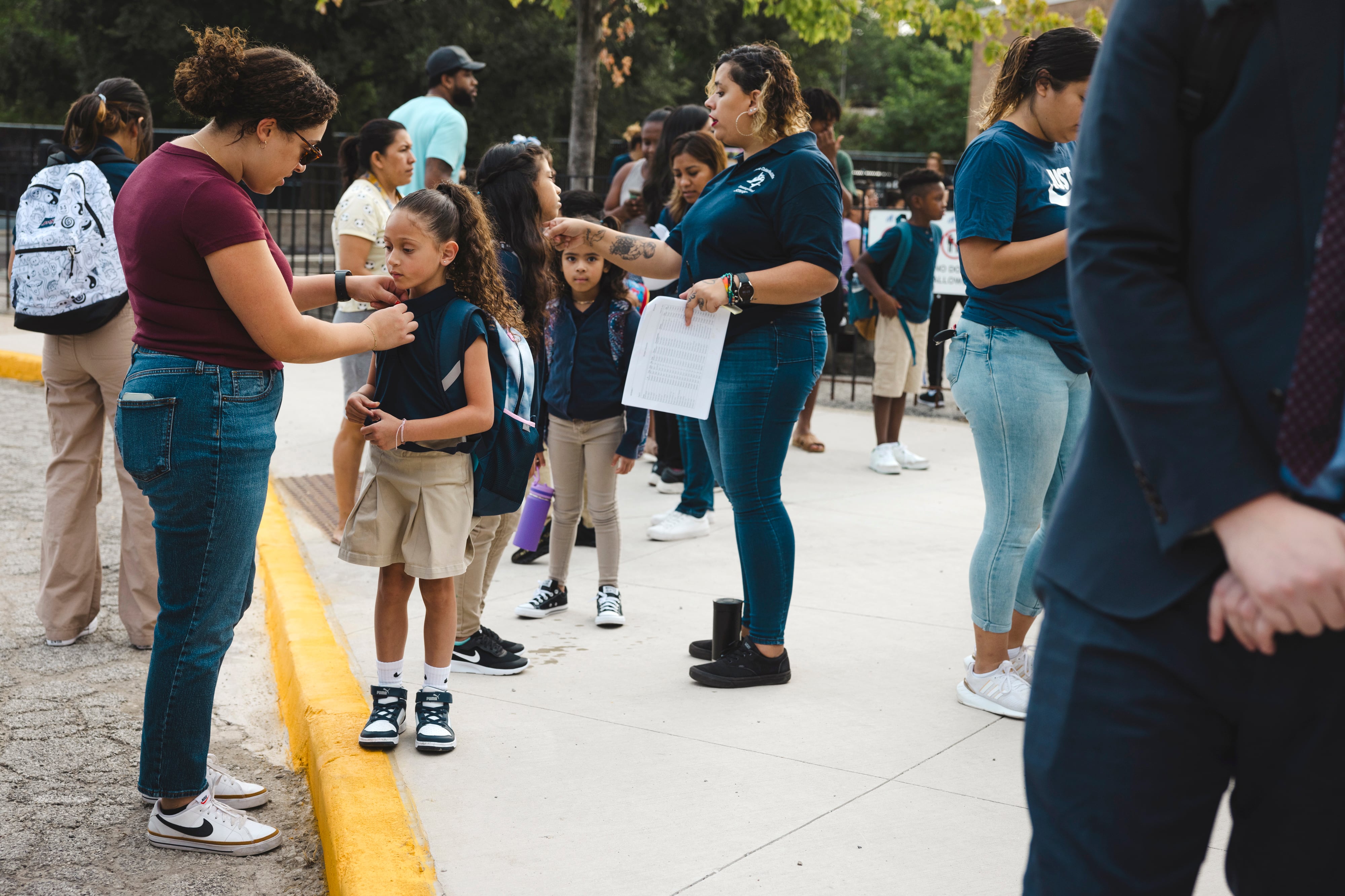 A group of students, families and staff stand outside a school.