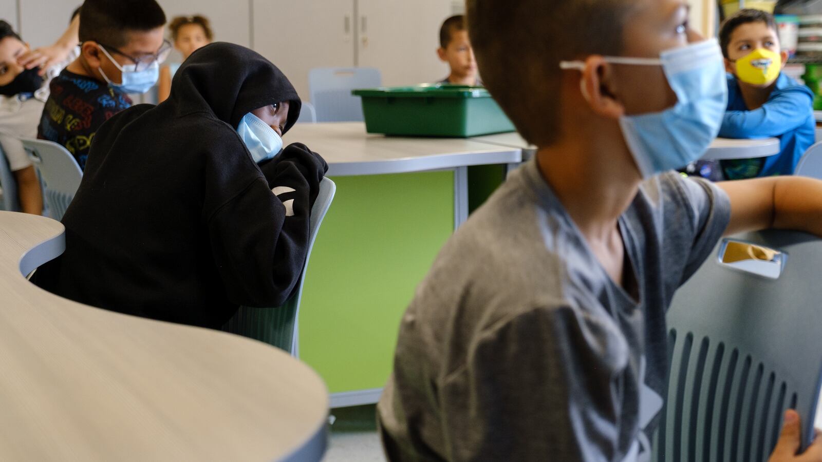 Students in masks listen in the classroom, some slumped over their chairs.