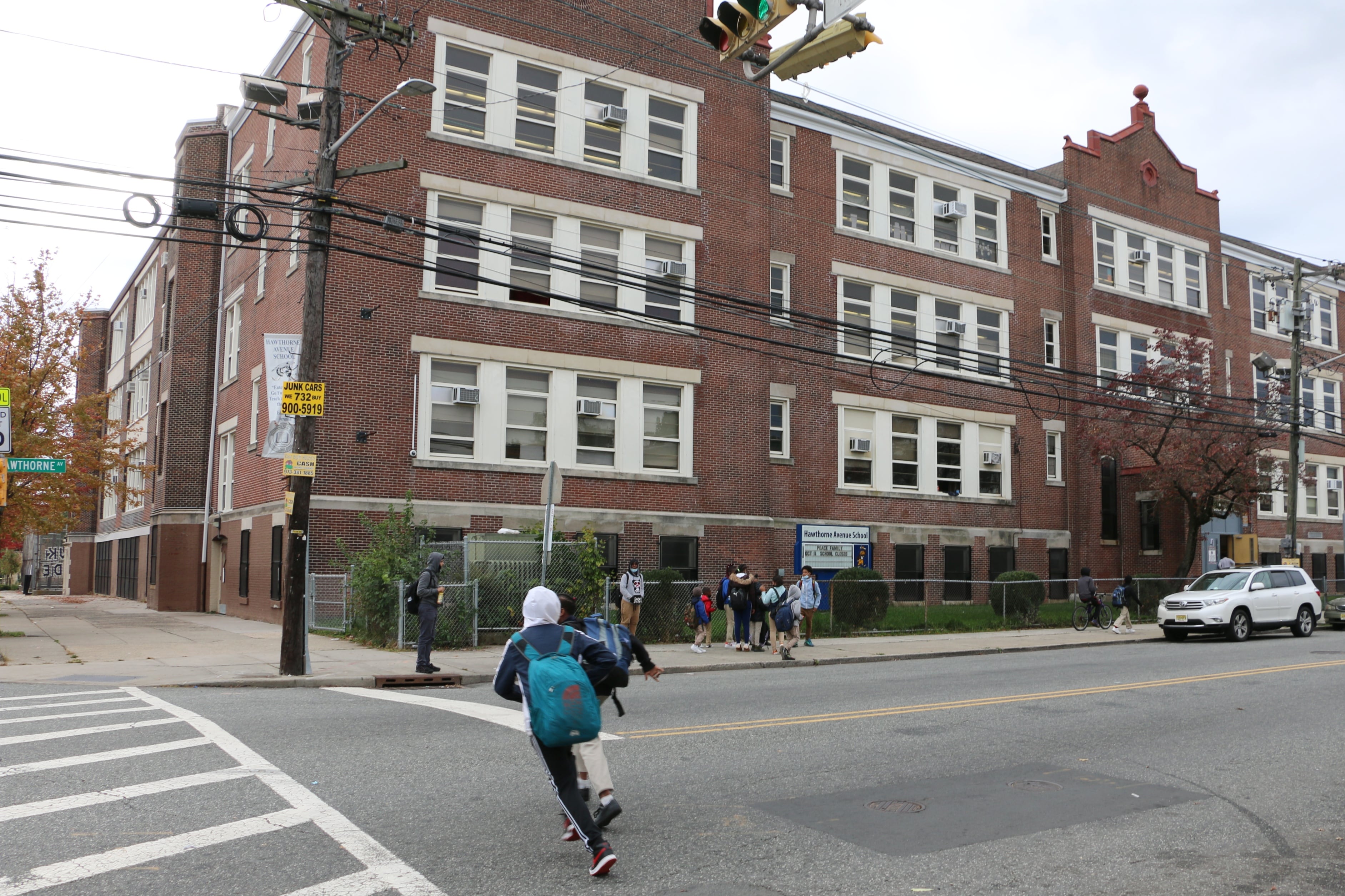 A boy with a blue backpack runs across the street in front of a school building in Newark.