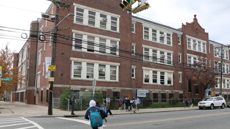 A boy with a blue backpack runs across the street in front of a school building in Newark.