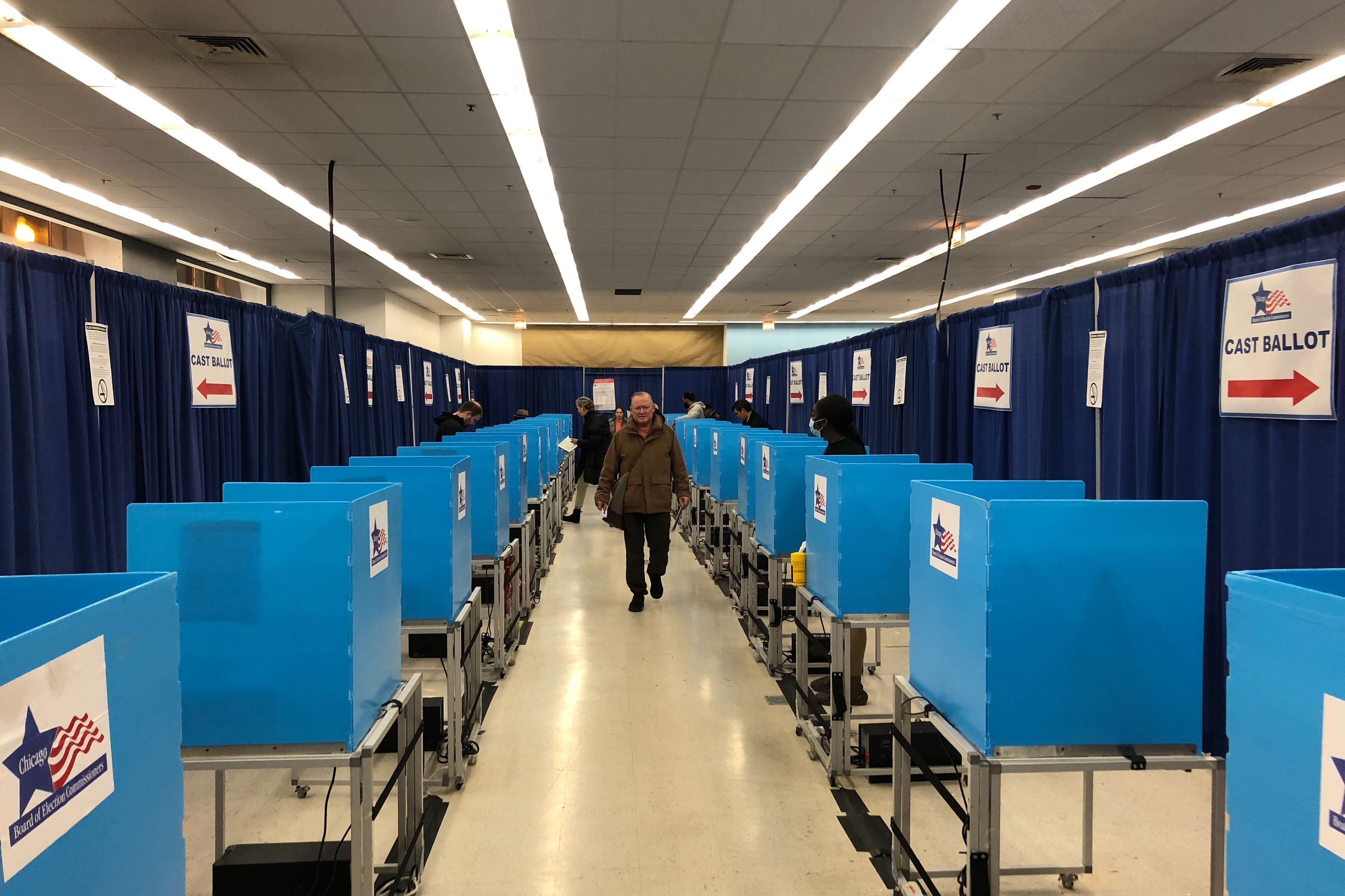 A person in a winter coat walks down a hallway of blue voting separators in a room.