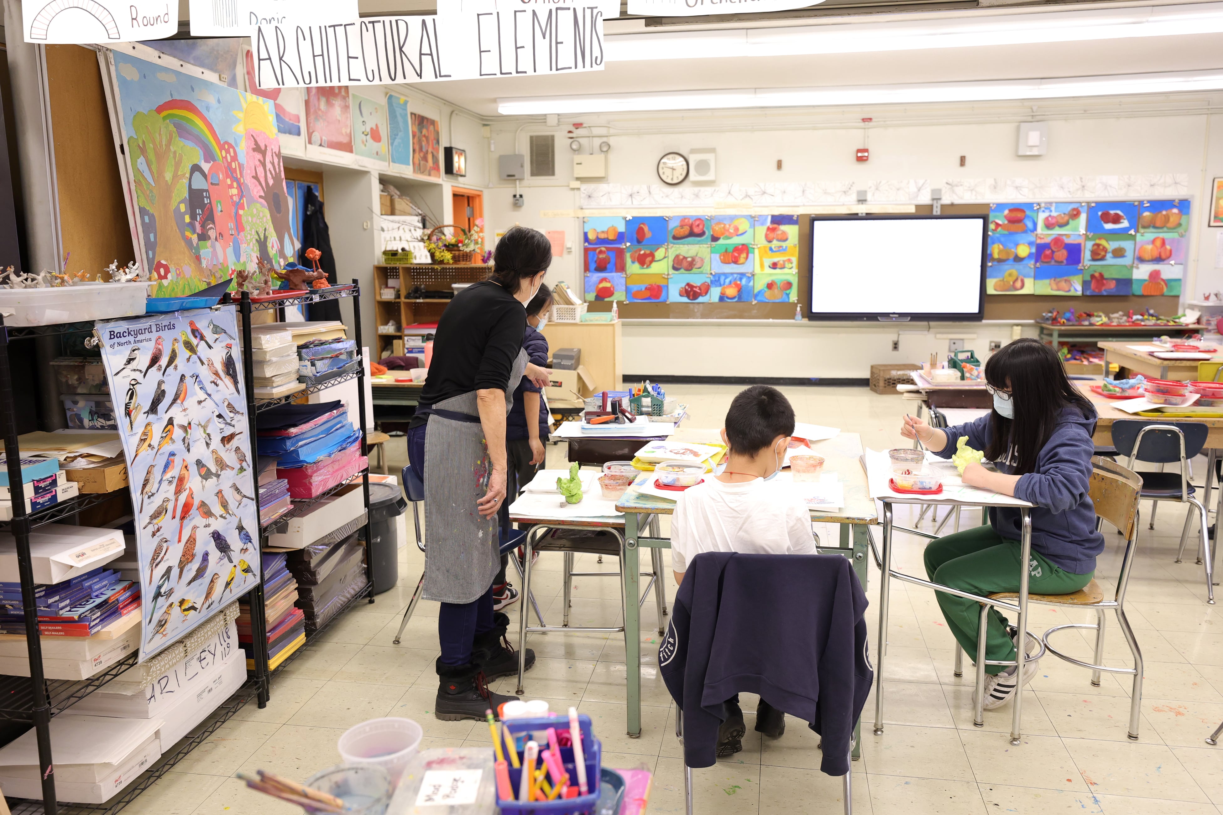 A person stands next to a table where two students are seated.