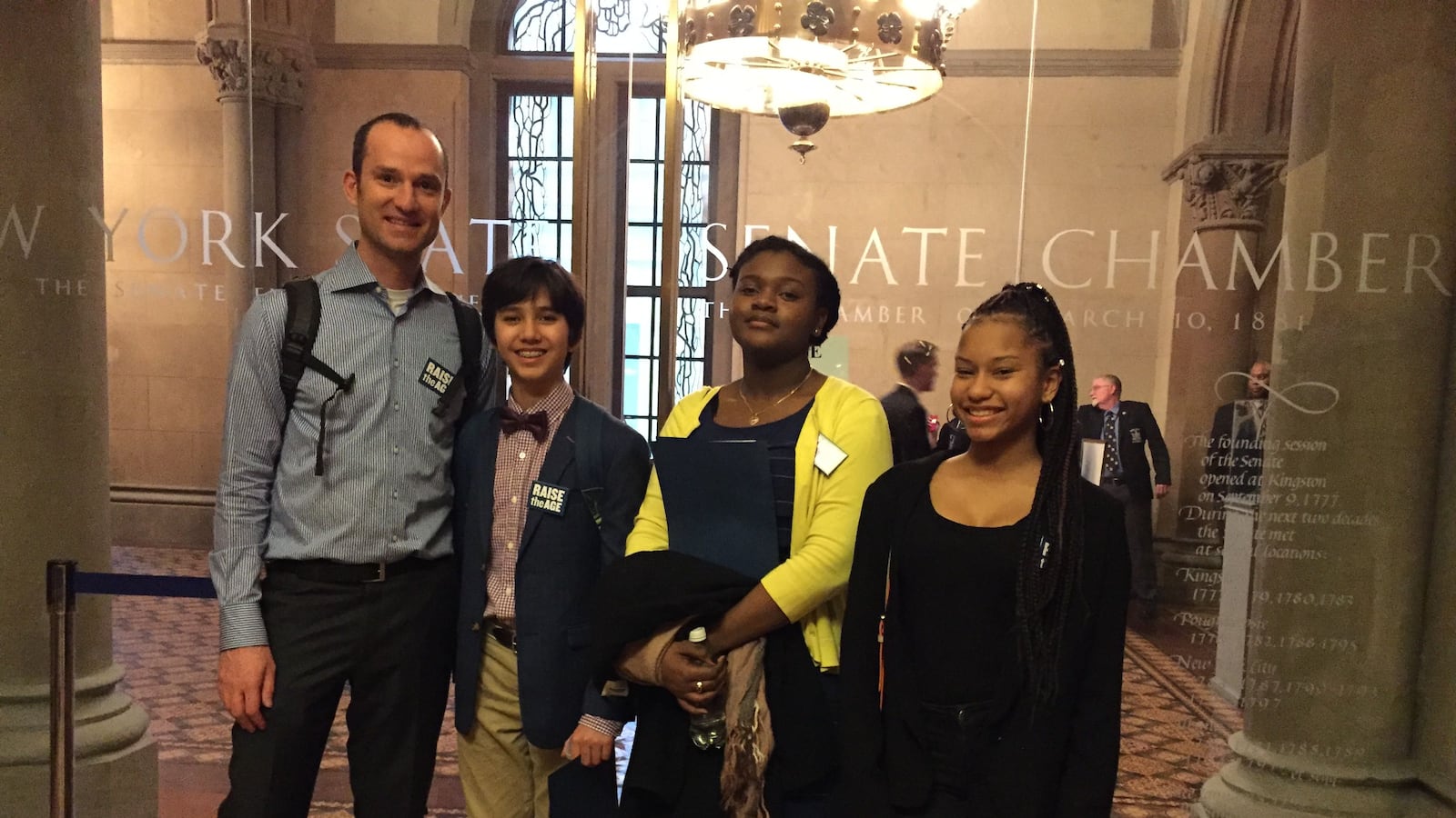 Assistant Principal Benjamin Geballe (left) poses outside the New York Senate chamber with students Dash Avincula (center left), Alex Bristol (center right) and Kayla Mowatt (right).