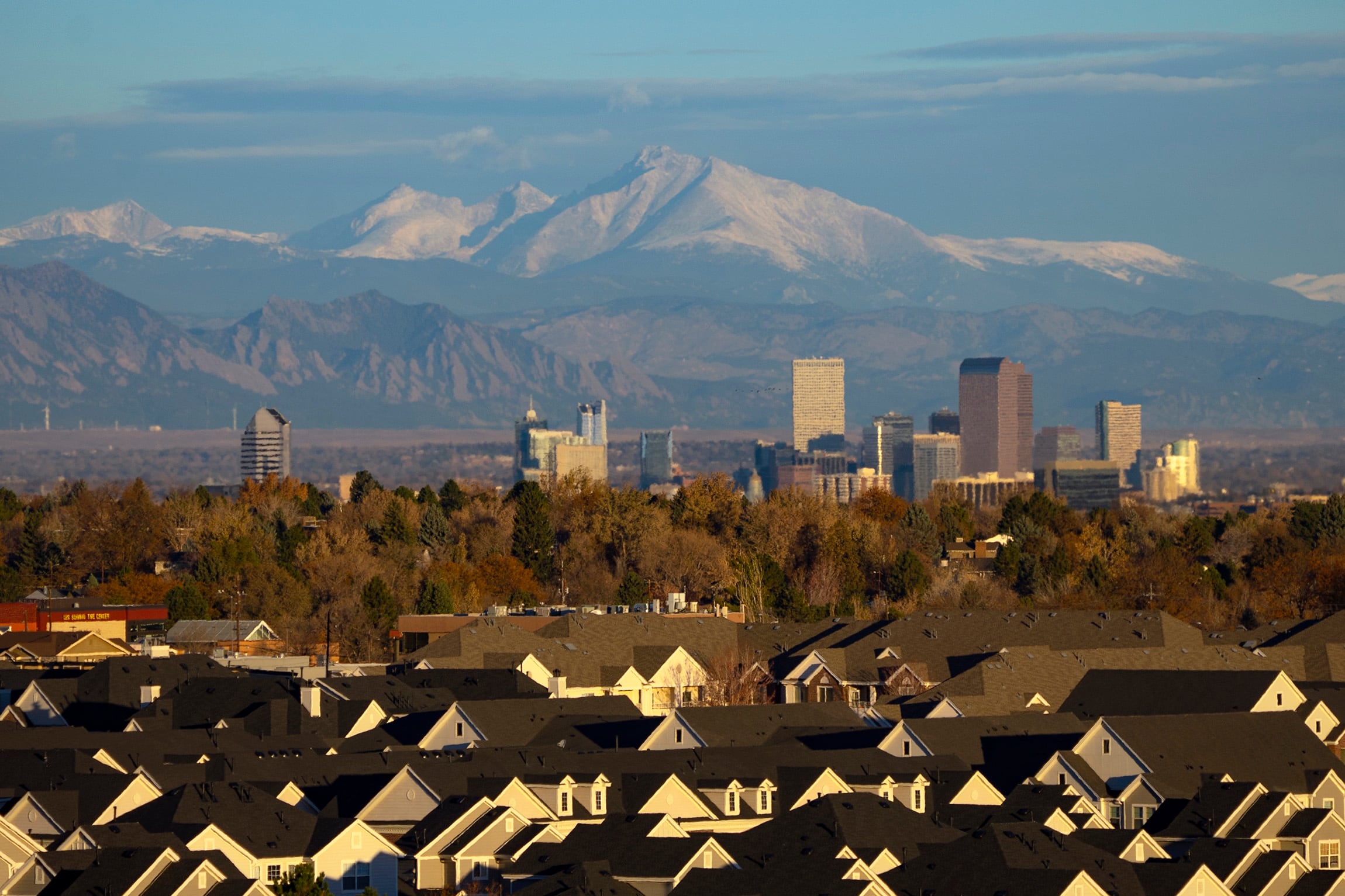 Mountains rise above the Denver skyline. In the foreground are the rooftops of residential development.