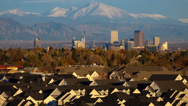 Mountains rise above the Denver skyline. In the foreground are the rooftops of residential development.