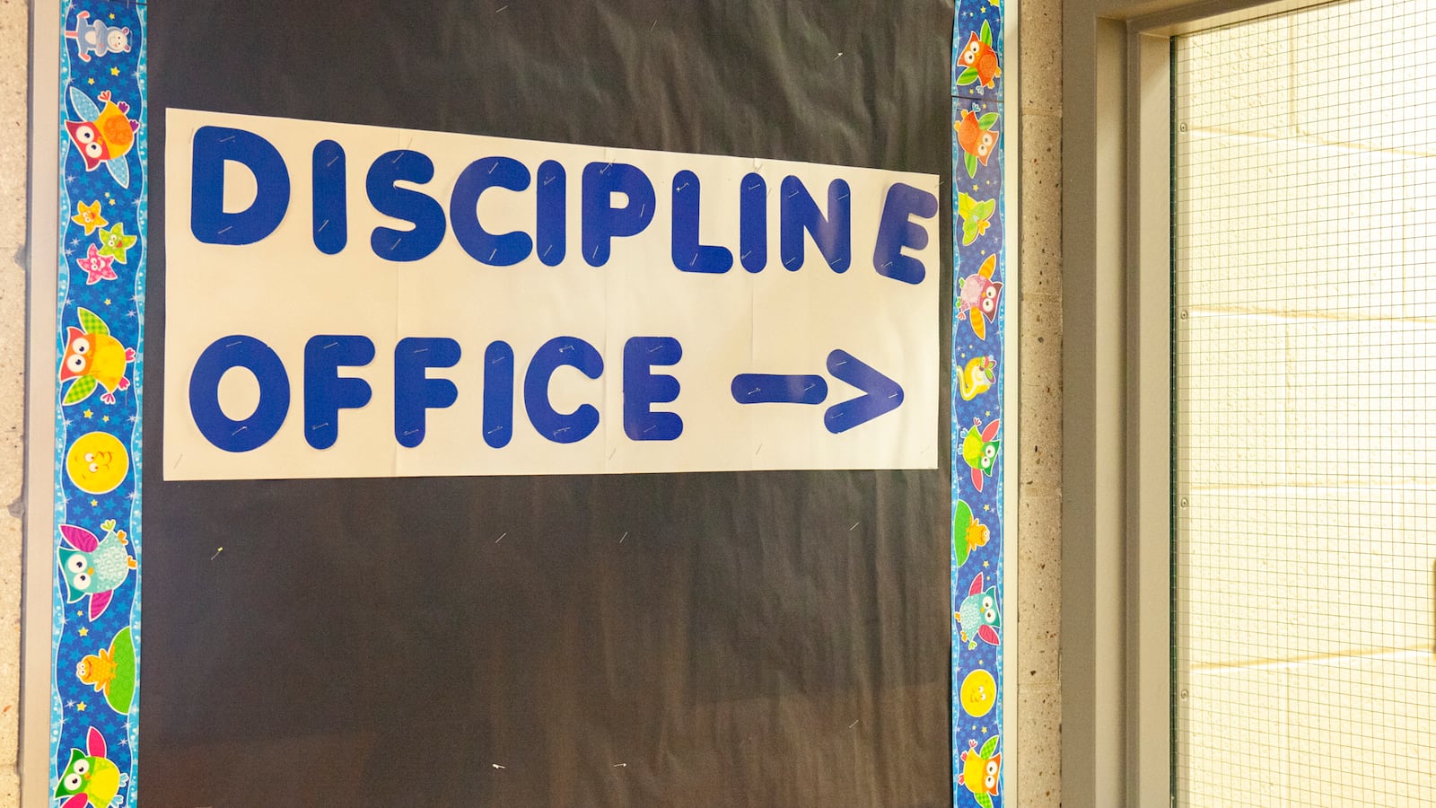 A sign reads “DISCIPLINE OFFICE” on a board with black paper next to a school office’s windows.