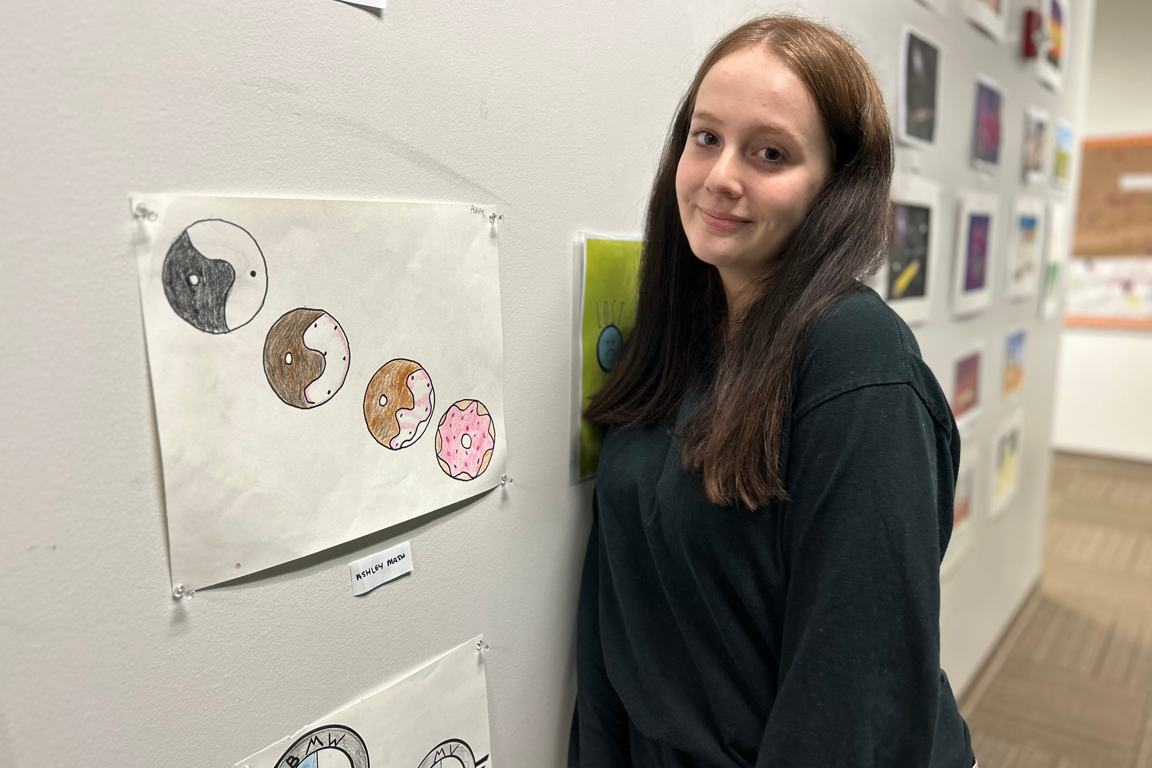 A student stands smiling in front of artwork she made.