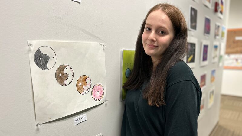 A student stands smiling in front of artwork she made.