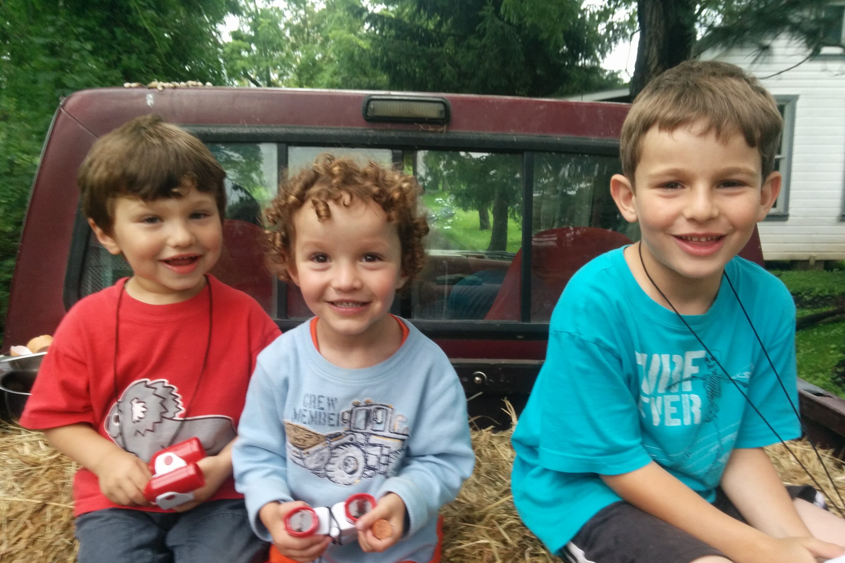 Three young boys sit on hay in the back of a pickup truck