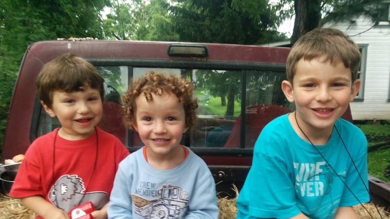 Three young boys sit on hay in the back of a pickup truck