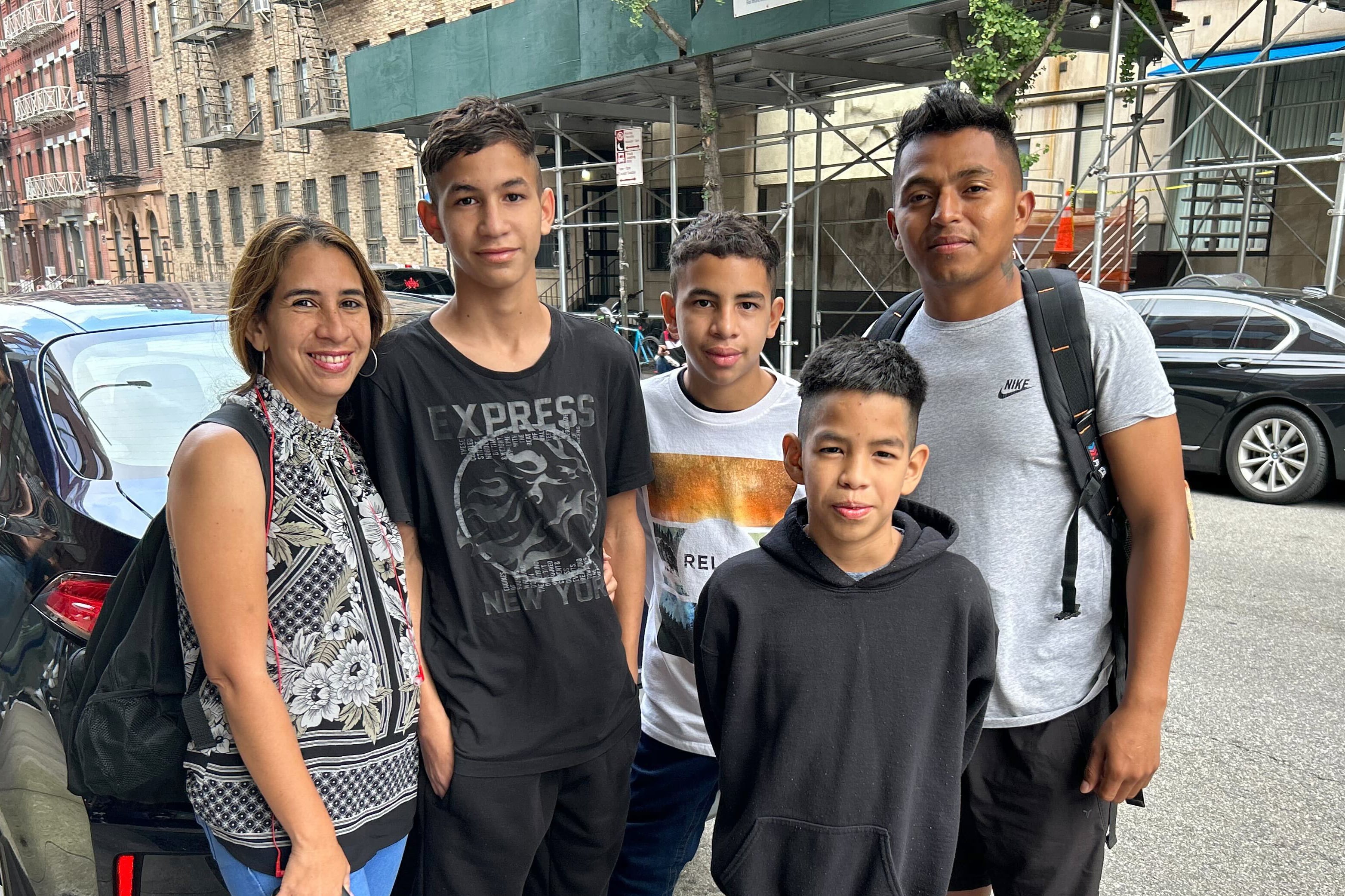 A family with a father, mother and three children stand in front of a car on a New York City street.