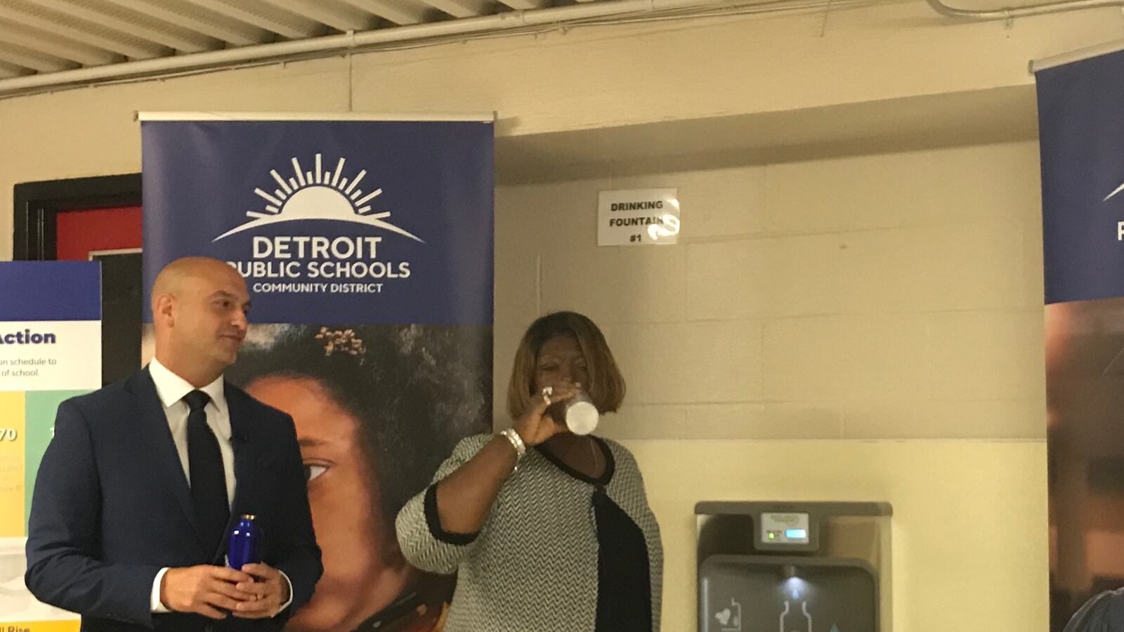 Superintendent Nikolai Vitti looks on as Iris Taylor, president of the Detroit school board, drinks from one of the more than 500 water hydration stations that have been installed in schools across the Detroit district.