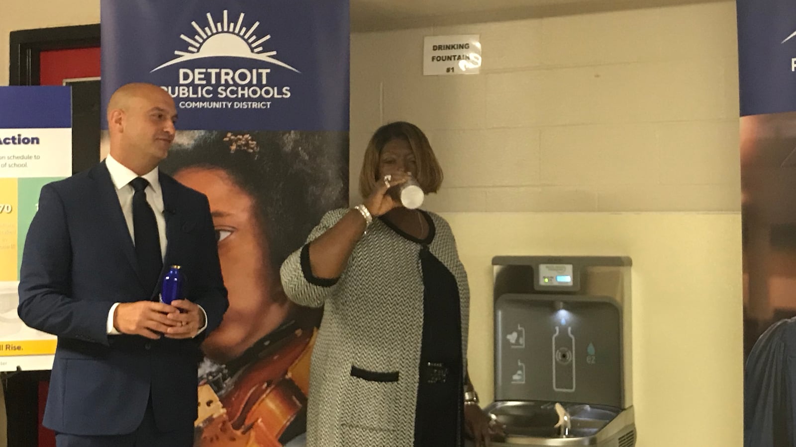 Superintendent Nikolai Vitti looks on as Iris Taylor, president of the Detroit school board, drinks from one of the more than 500 water hydration stations that have been installed in schools across the Detroit district.