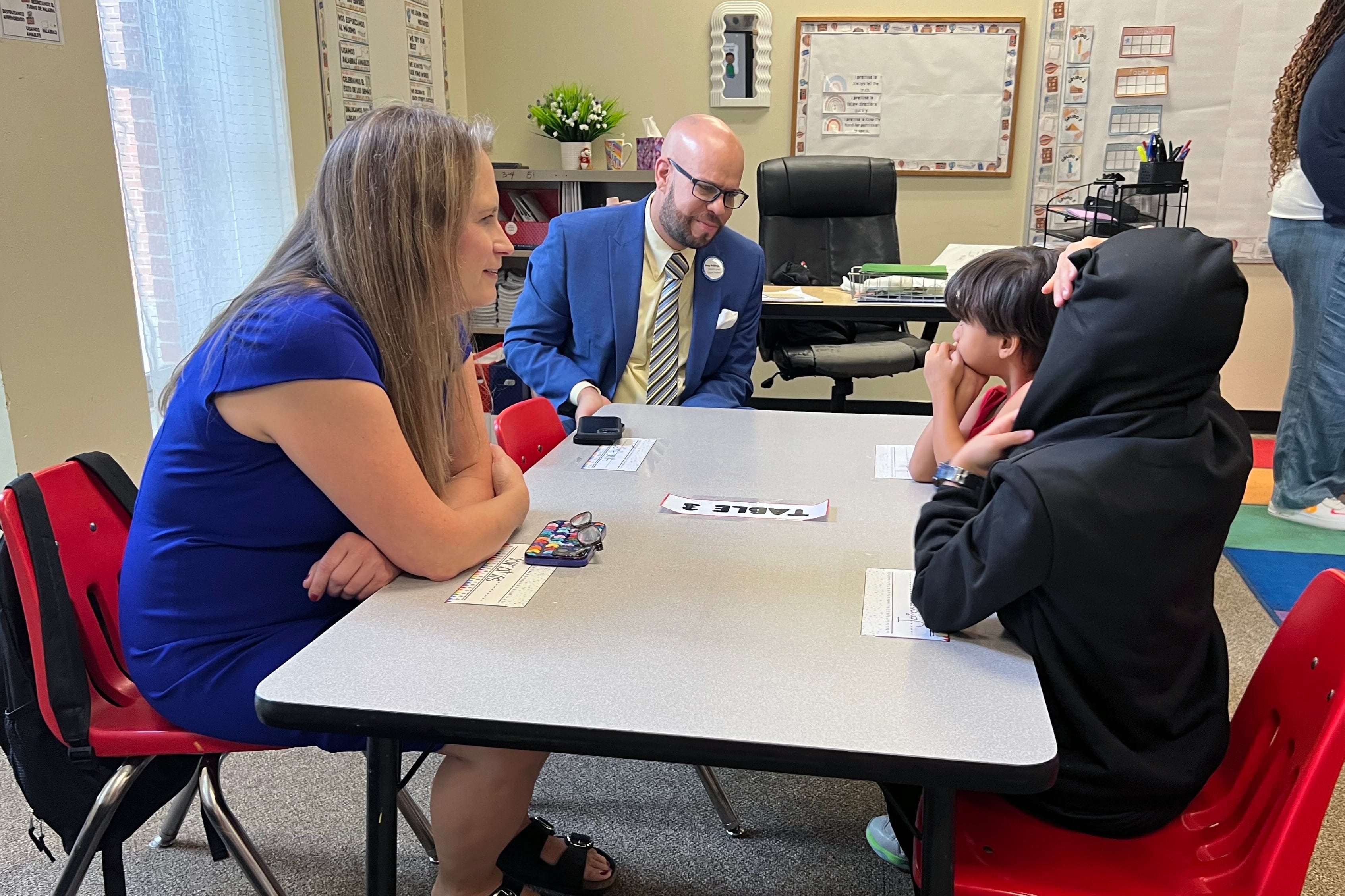 Two adults and two young students sit at a table in a classroom.