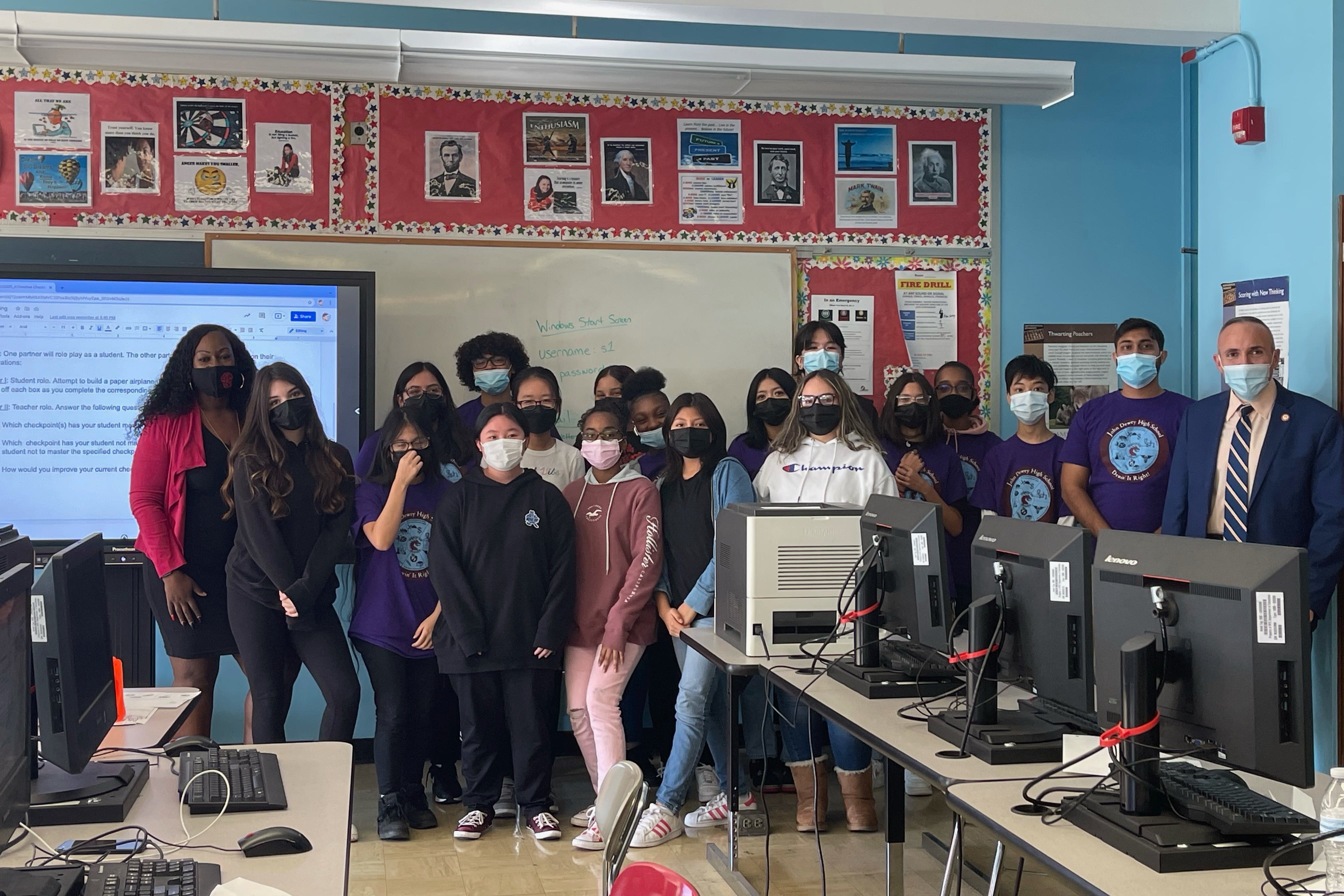 A group of students wearing masks stand inside a classroom.
