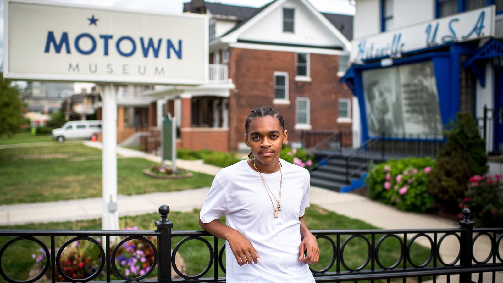 King Bethel, wearing a white shirt and gold necklaces, leans against a railing outside of Detroit’s Motown Museum.