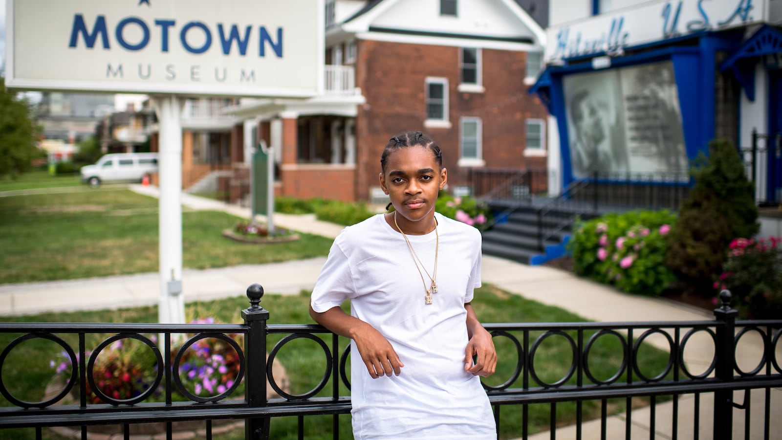 King Bethel, wearing a white shirt and gold necklaces, leans against a railing outside of Detroit’s Motown Museum.