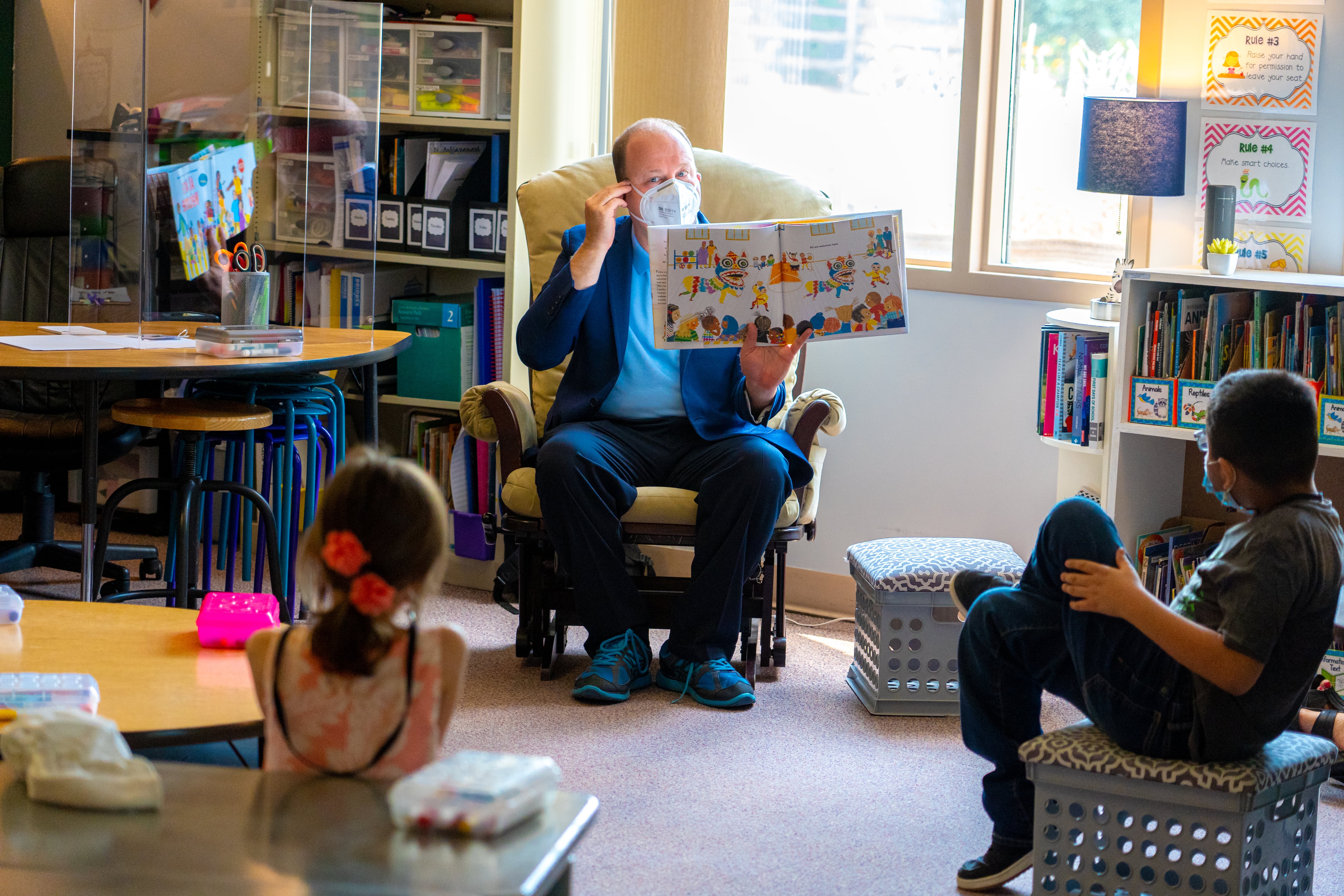 Colorado Gov. Jared Polis reads a story to young schoolchildren in a classroom while wearing a mask during the COVID-19 pandemic.