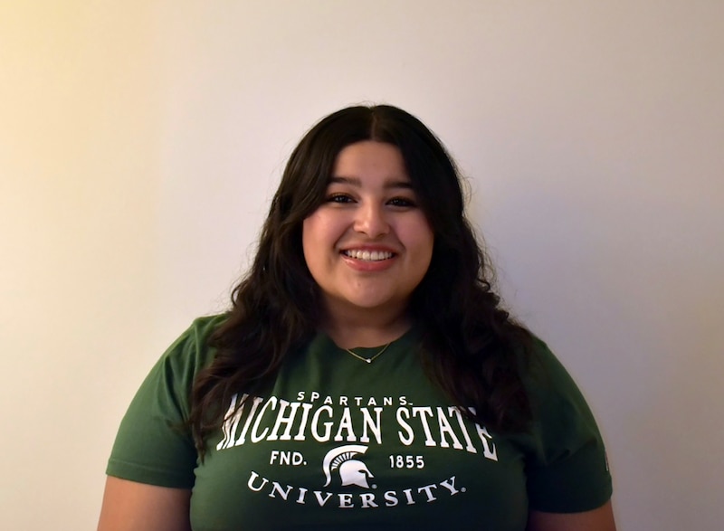 A high school girl poses for a portrait with a green Michigan State University t-shirt.