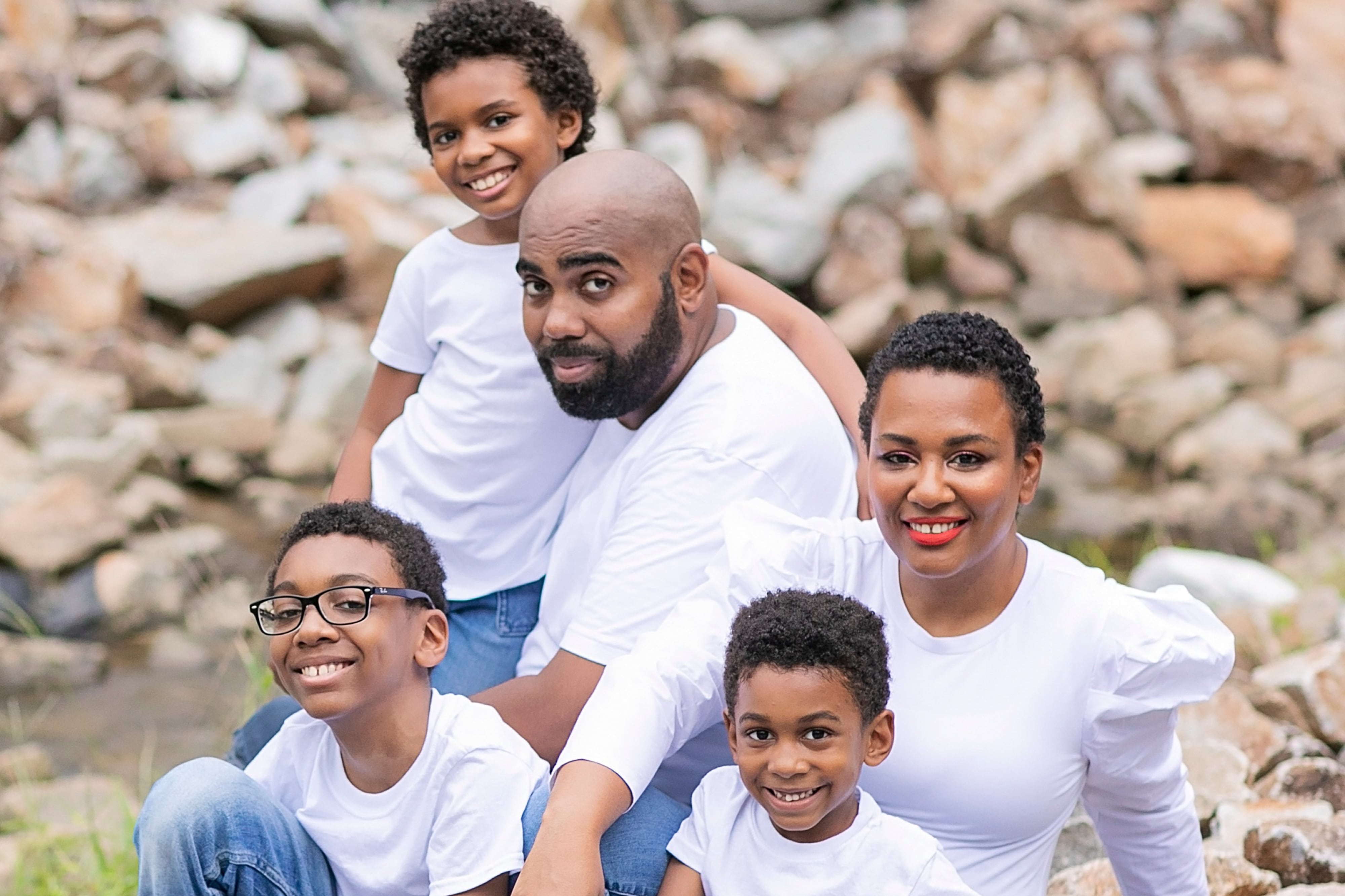 A father, mother and three boys pose for a portrait outside in front of some rocks. All of the family members are wearing white.