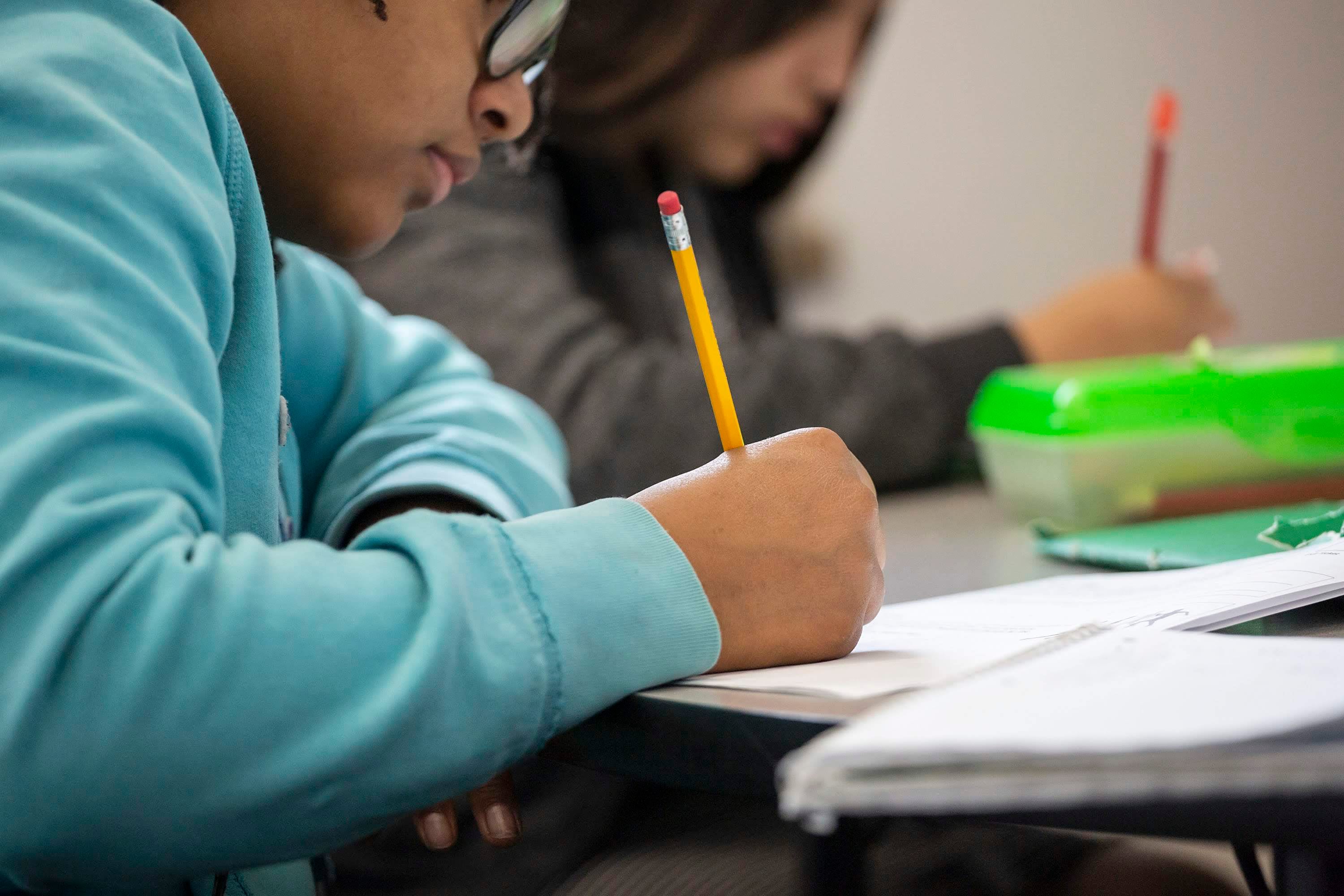 A close up image of two students sitting next to each other while writing with pencils.