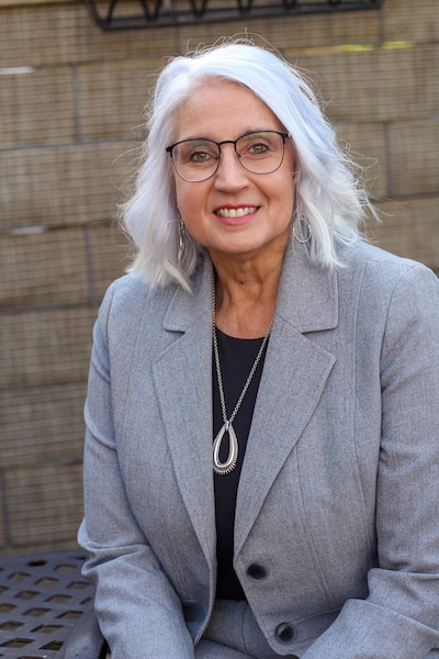 A woman wearing glasses and a gray blazer with shoulder-length white hair.