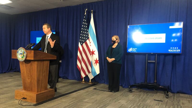 Standing at a podium in a suit and tie, Chicago Public Schools CEO Pedro Martinez explains the new quarantine rules alongside Dr. Allison Arwady, the city’s top health official.