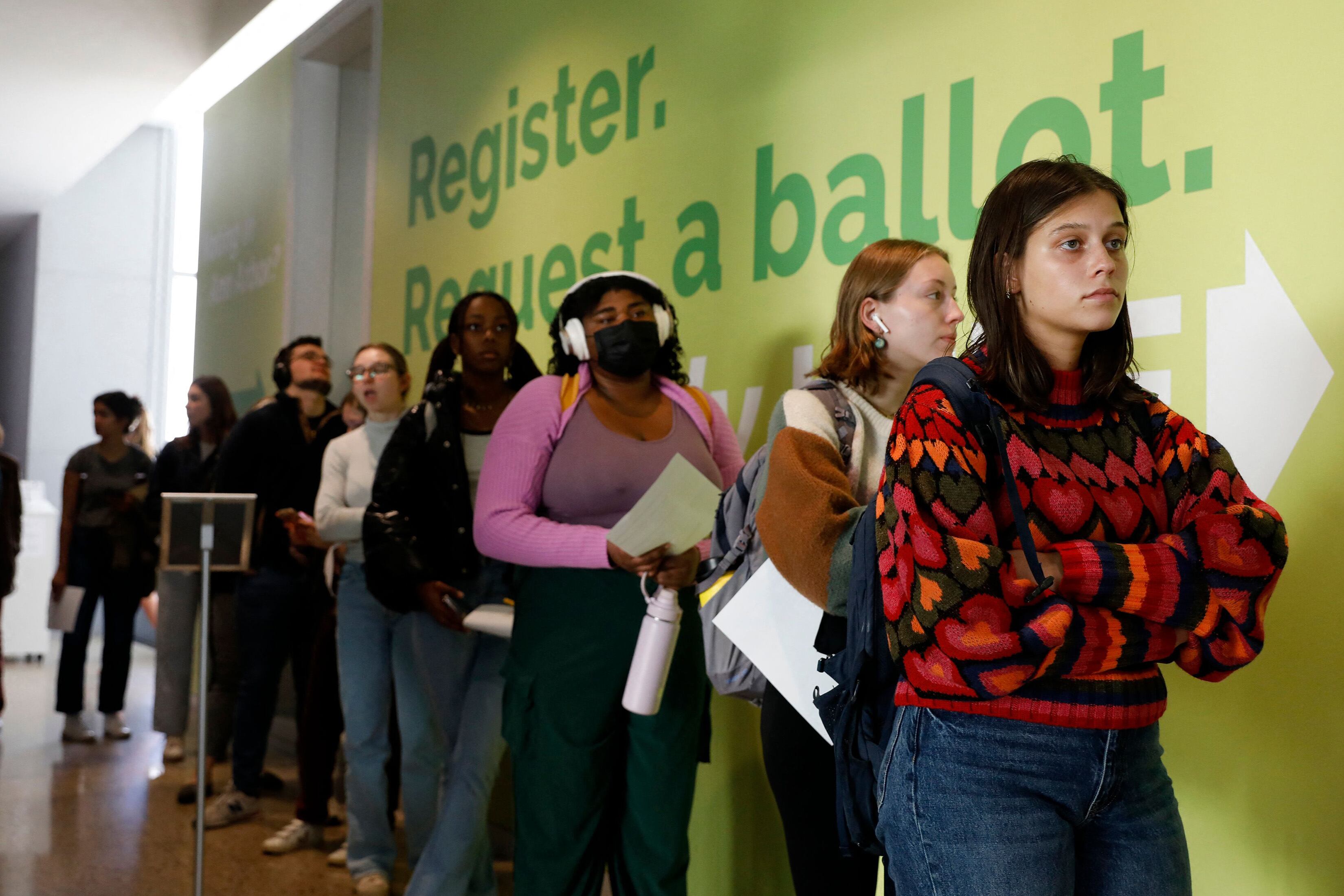 A line of college students against a green wall in a school hallway.