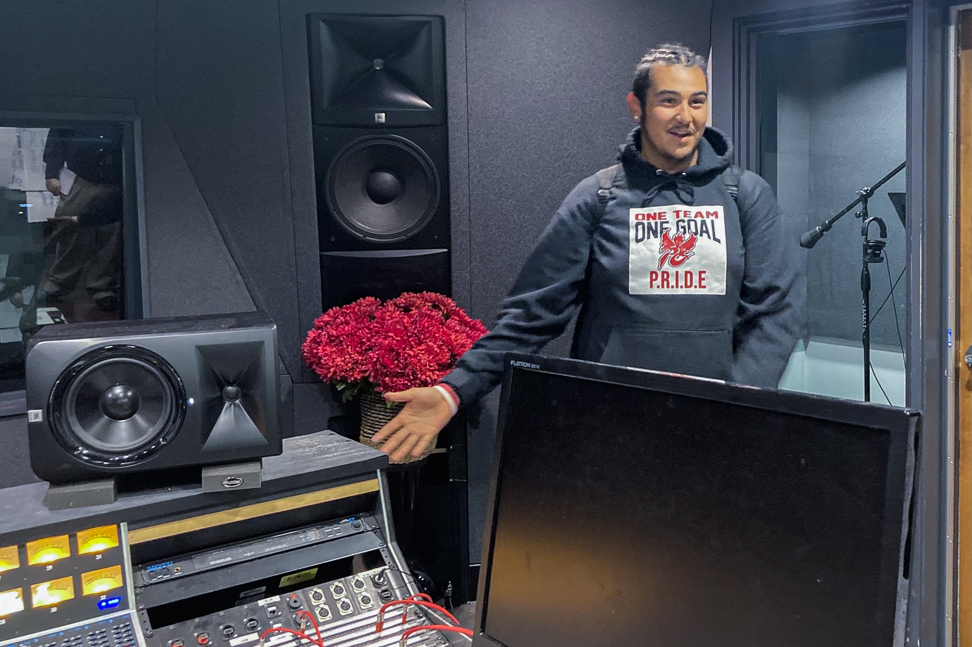 A teenage boy in a hoodie stands by recording studio equipment.