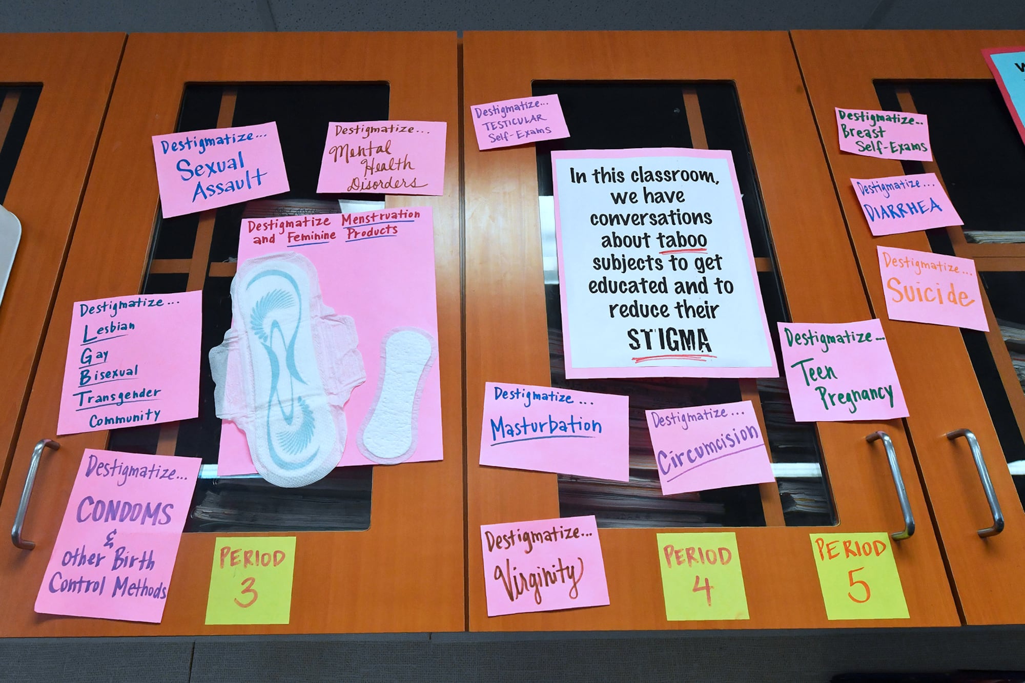 A photograph of wooden doors with pink and green sticky notes and posters.