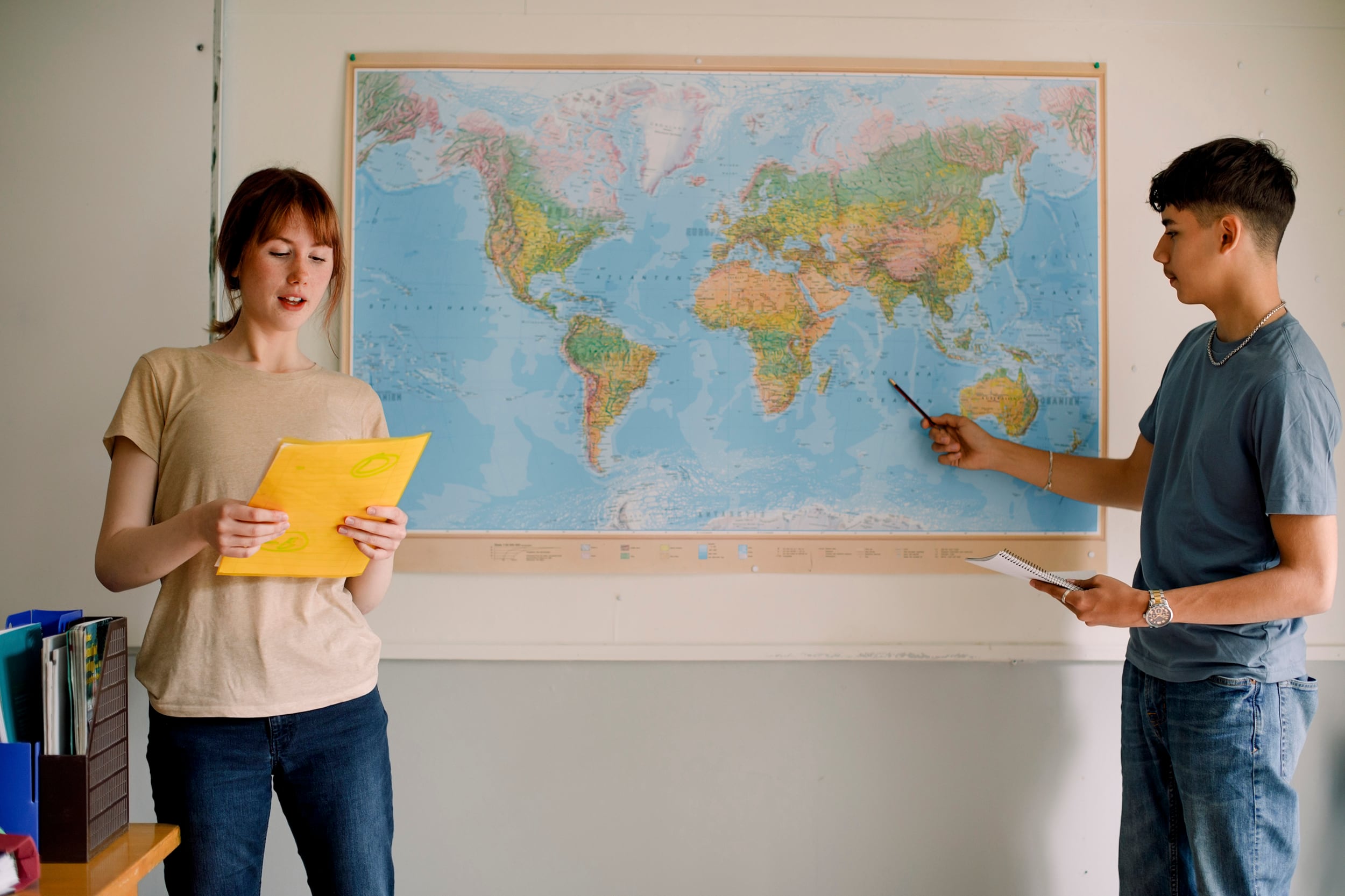 Two students stand in front of a world map with a white background.