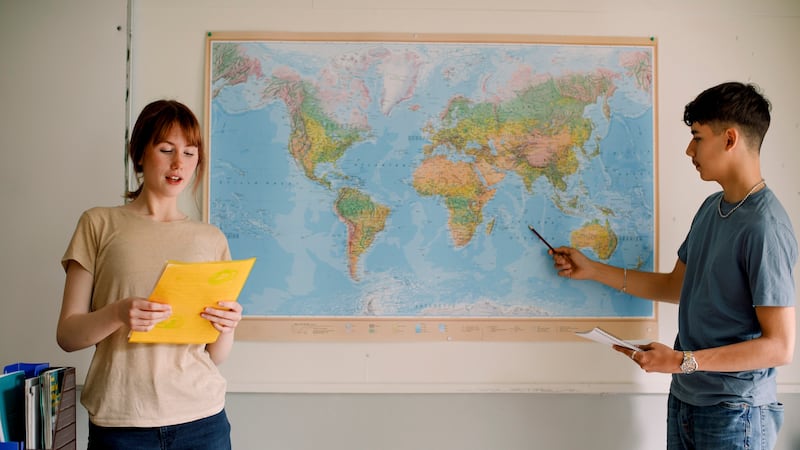 Two students stand in front of a world map with a white background.