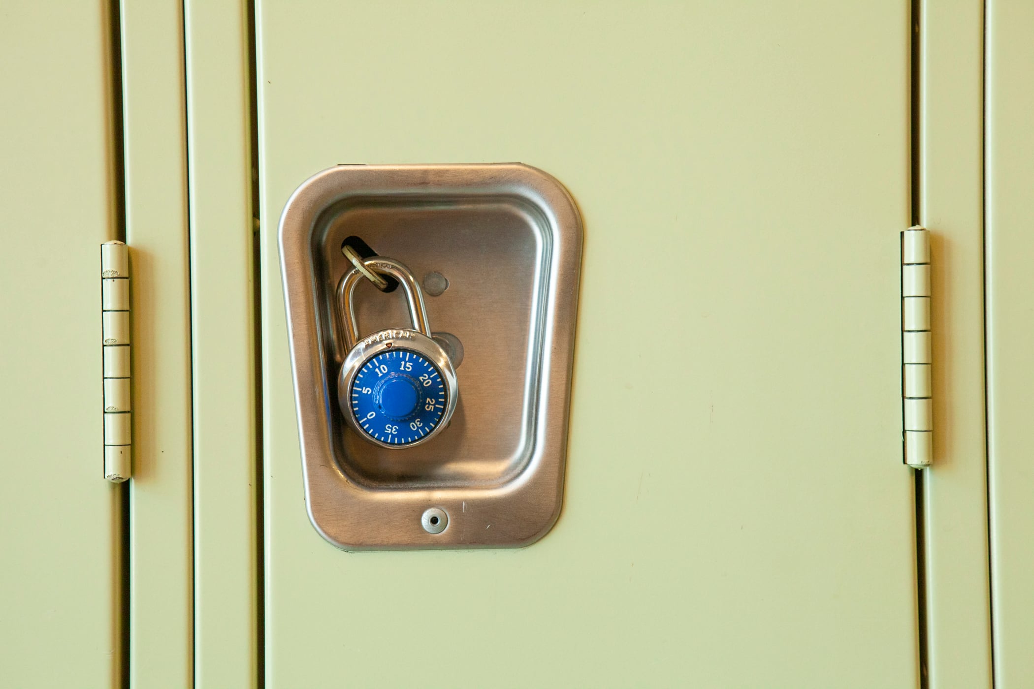 A close of image of a yellow high school locker with a blue pad lock. 