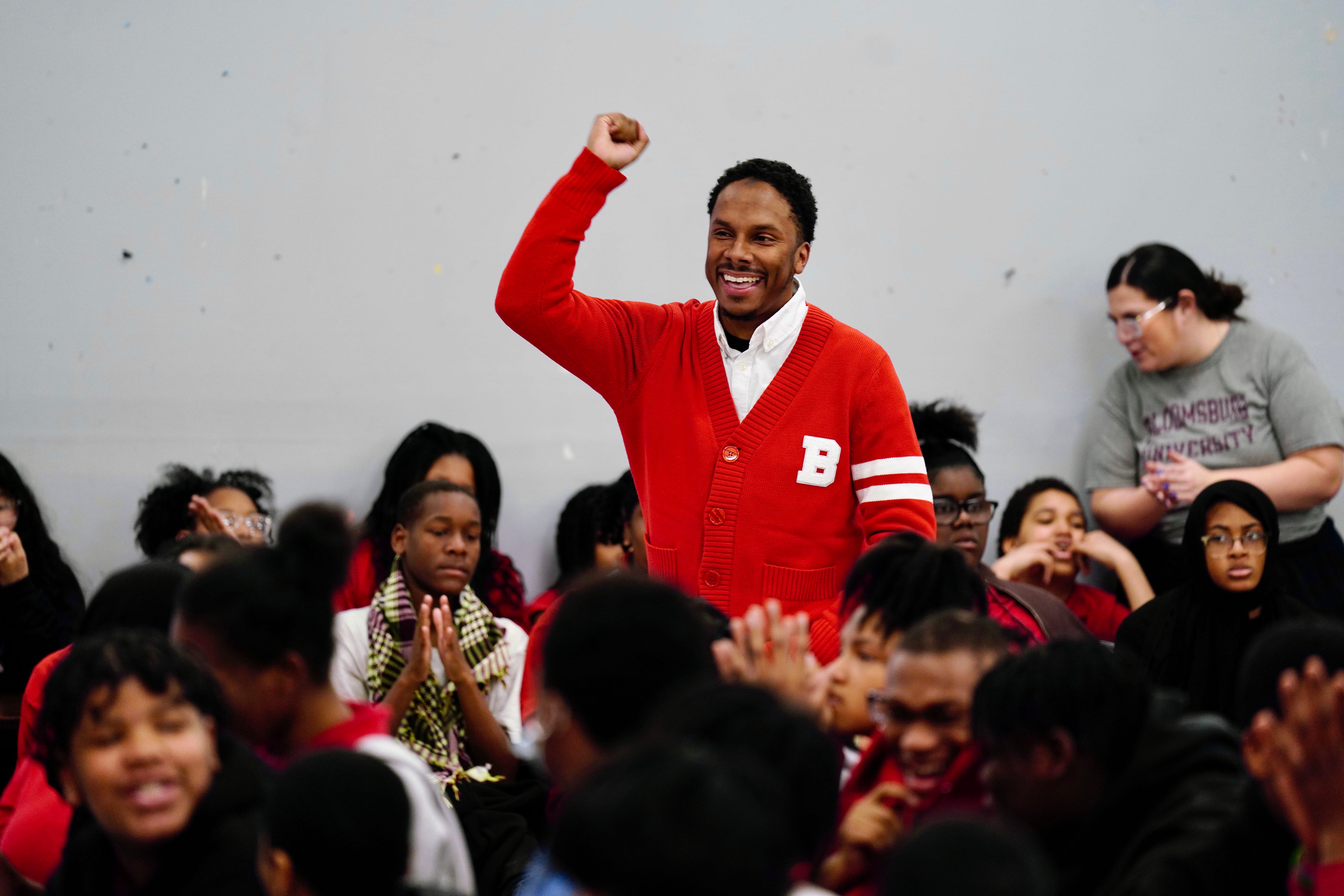 A man with short dark hair and wearing a red sweater stands above a crowd while pumping his fist in the air while celebrating with a big smile.