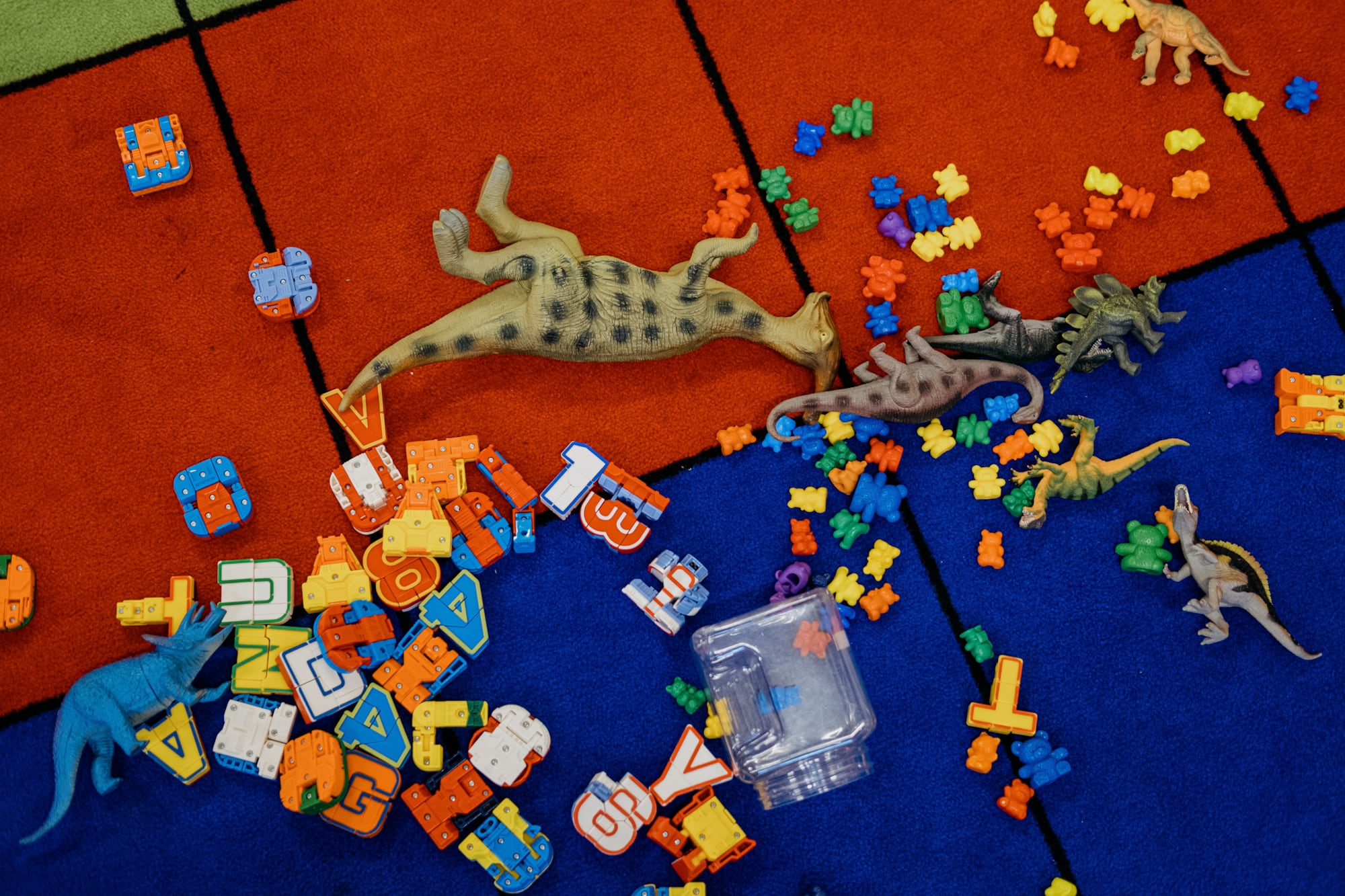 Dinosaur figures, alphabet blocks and small colorful toys sit on a colorful rug.